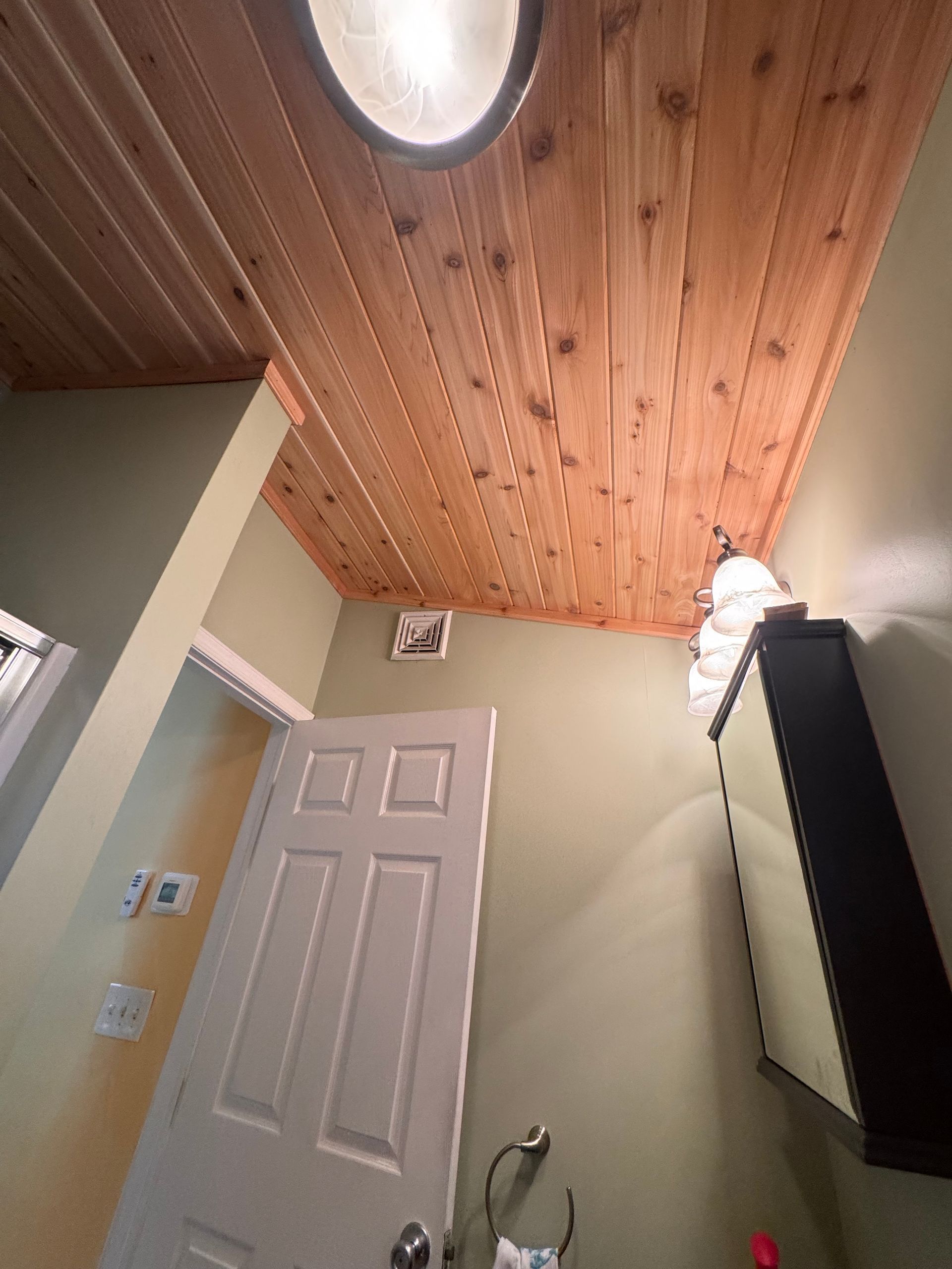 Bathroom with wood plank ceiling, white door, and light fixture. Green walls.