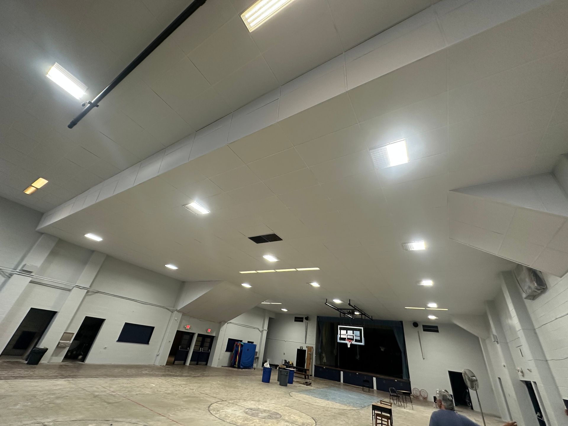 Wide-angle shot of a large, empty, white-walled room with ceiling lights and a basketball hoop on a dark wall.