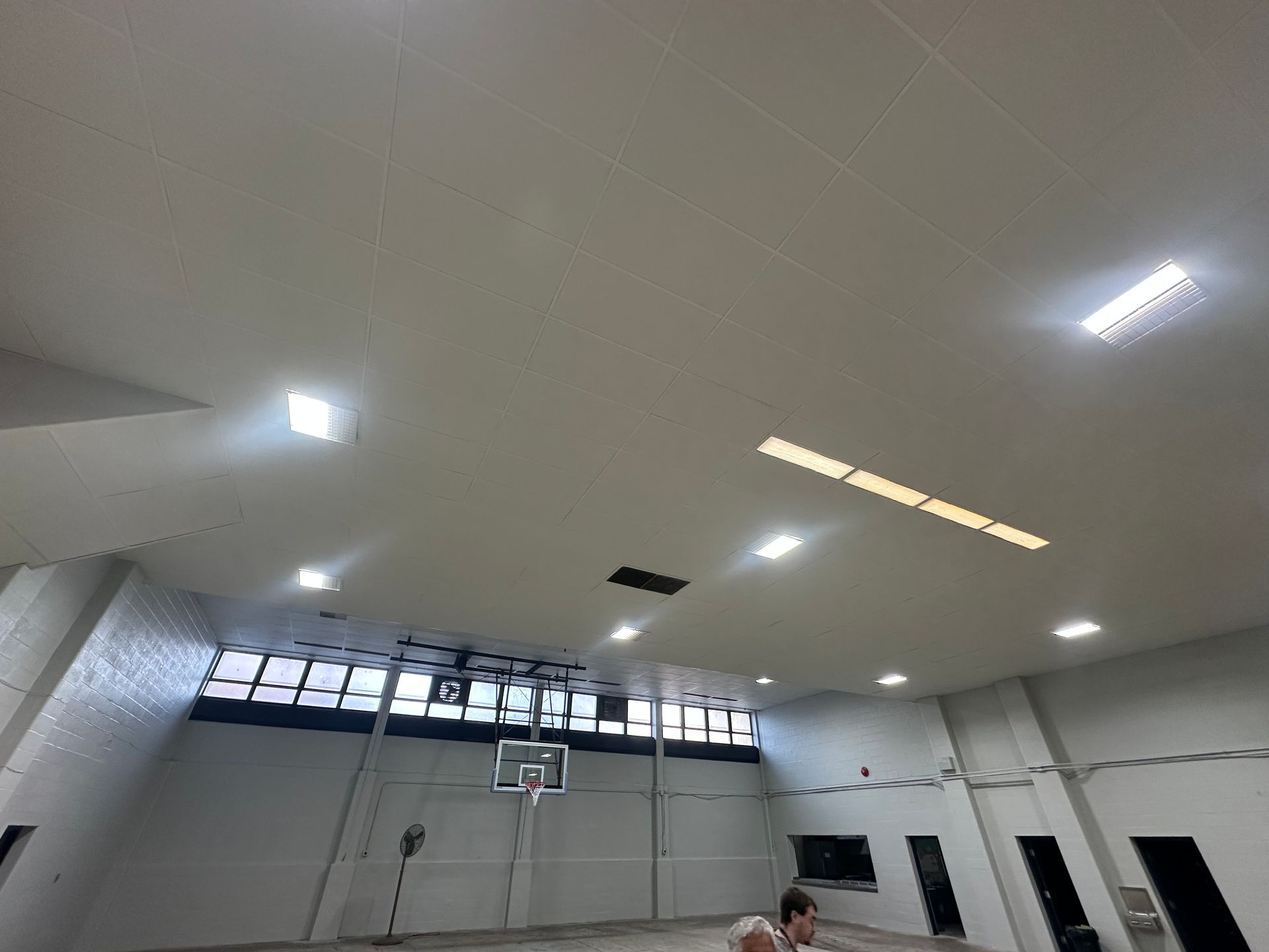 Basketball player in a gym, shooting towards the hoop. Bright lights illuminate the ceiling.