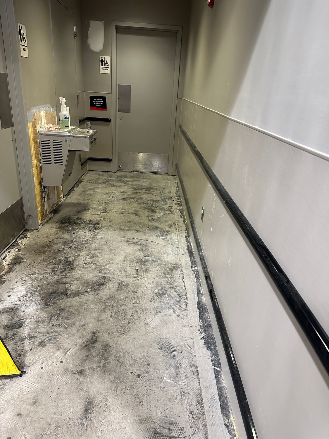 Narrow hallway with dirty floor, water fountain, and handrail. Door at end of hall.