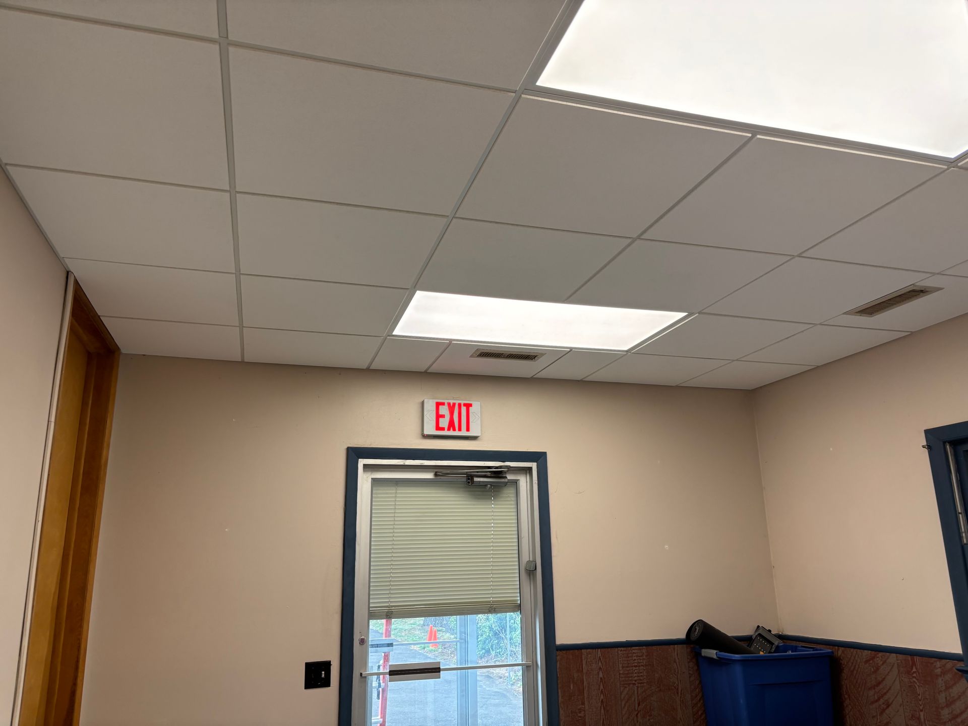 Ceiling tiles, exit sign above a door, beige walls.