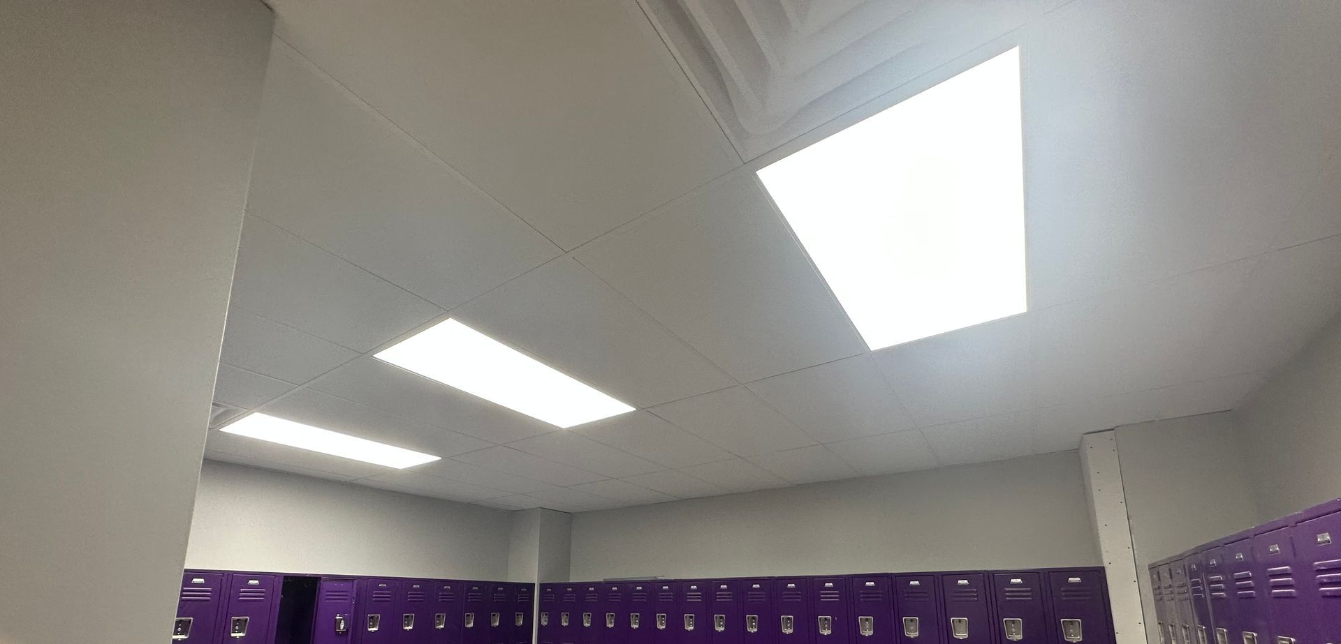 Ceiling of a room with bright rectangular lights and rows of purple lockers.