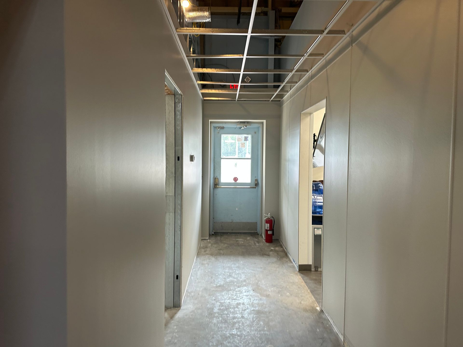 Interior hallway under construction with unfinished ceiling and closed door.