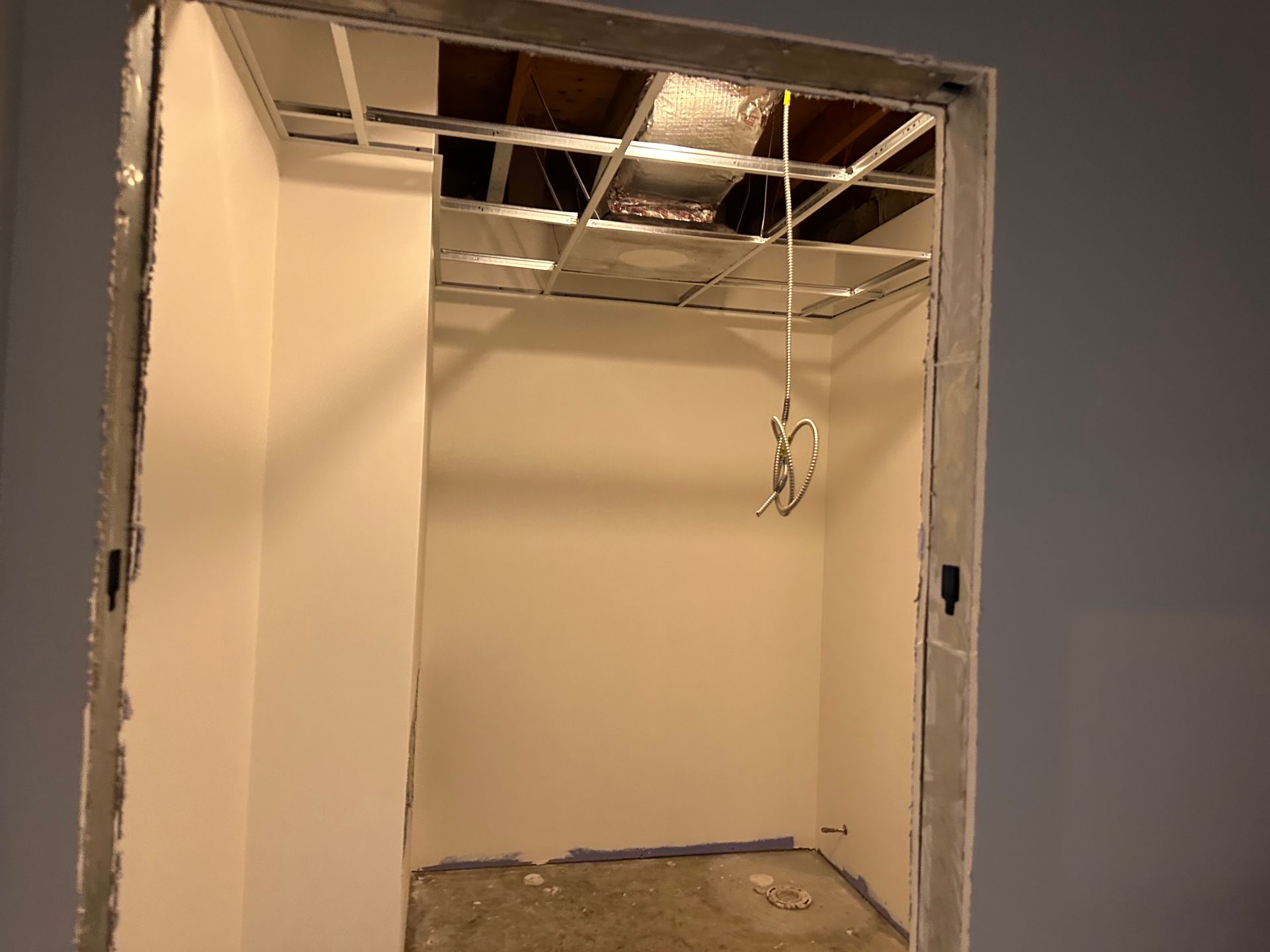 Interior wall under construction with exposed ceiling grid and hanging fixture.