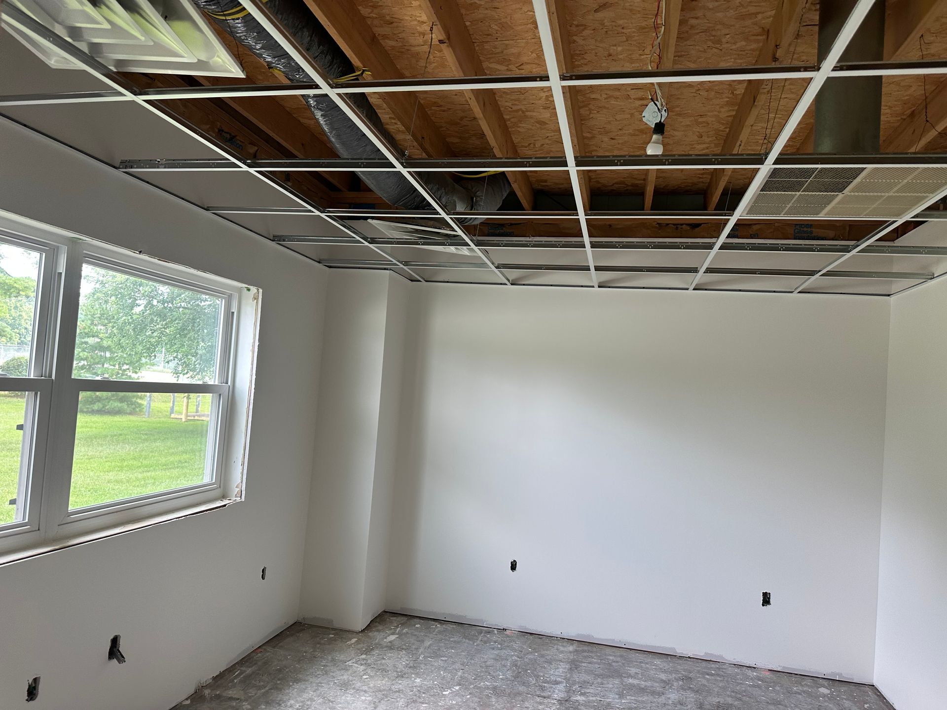 Room under construction with unfinished ceiling, white walls, and a window.