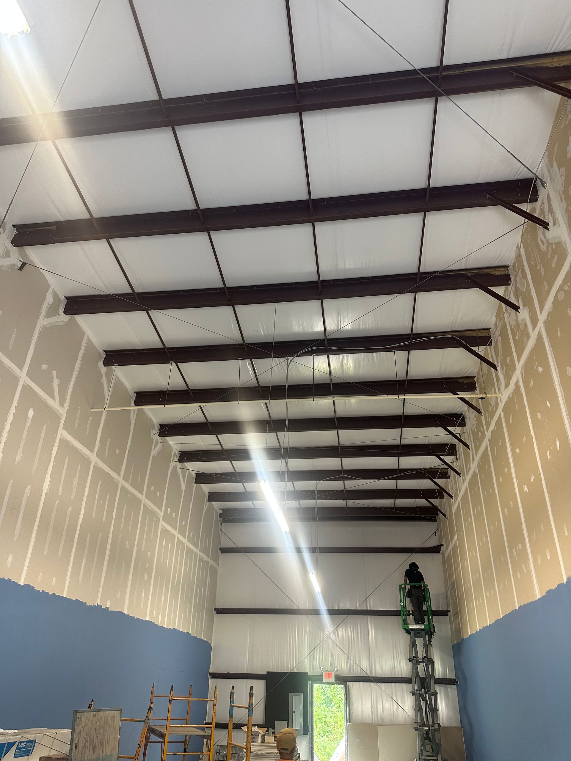Interior of a building under construction. A worker on a ladder, with exposed ceiling beams and partially finished walls.