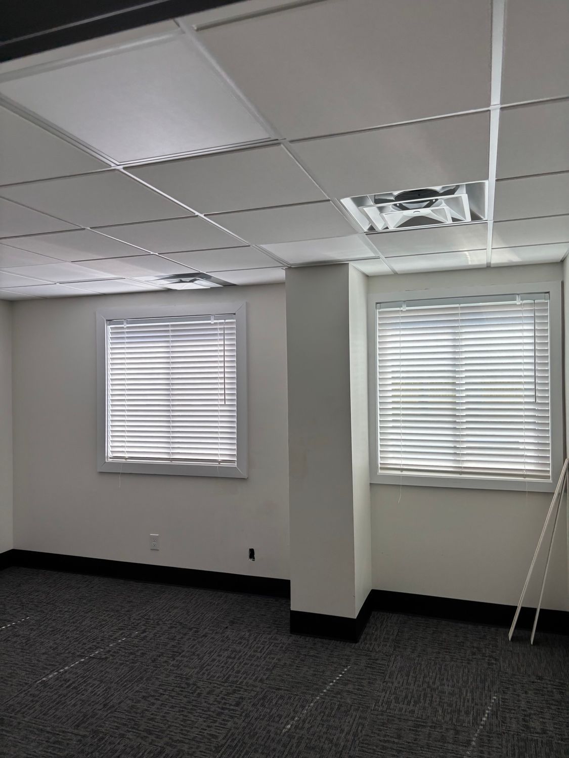 Empty office interior with two windows, a white pillar, and dark carpet.