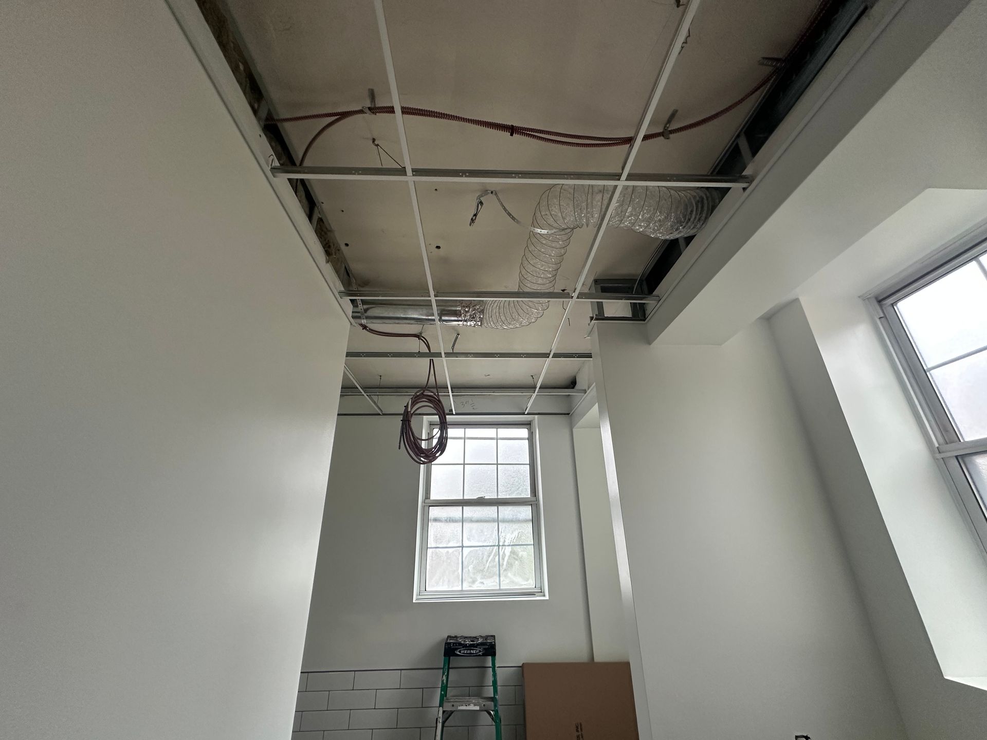 Interior room with unfinished ceiling, wiring, and a window. White walls and a ladder are visible.