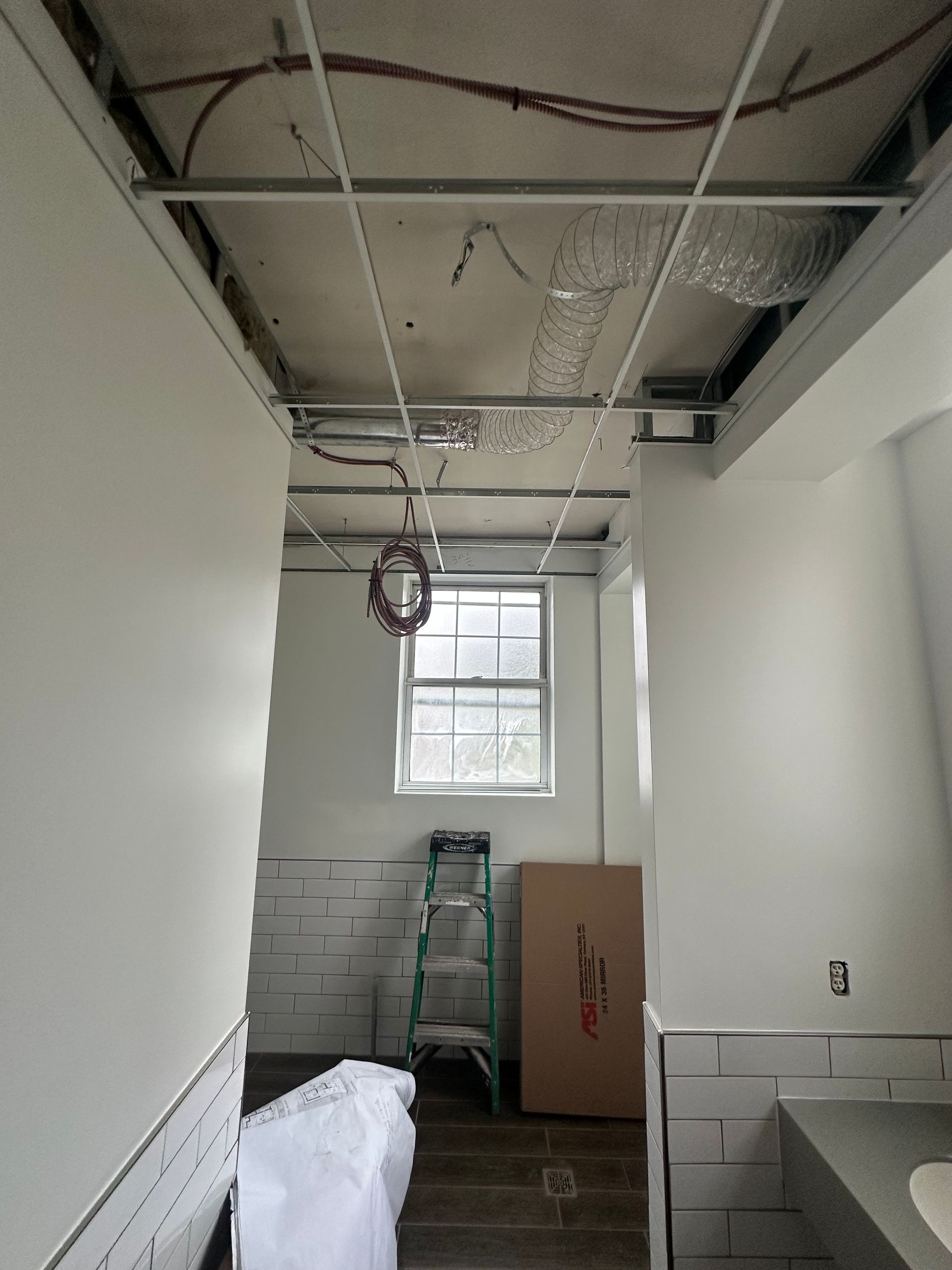 Construction site interior with exposed ceiling grid, walls, and window.