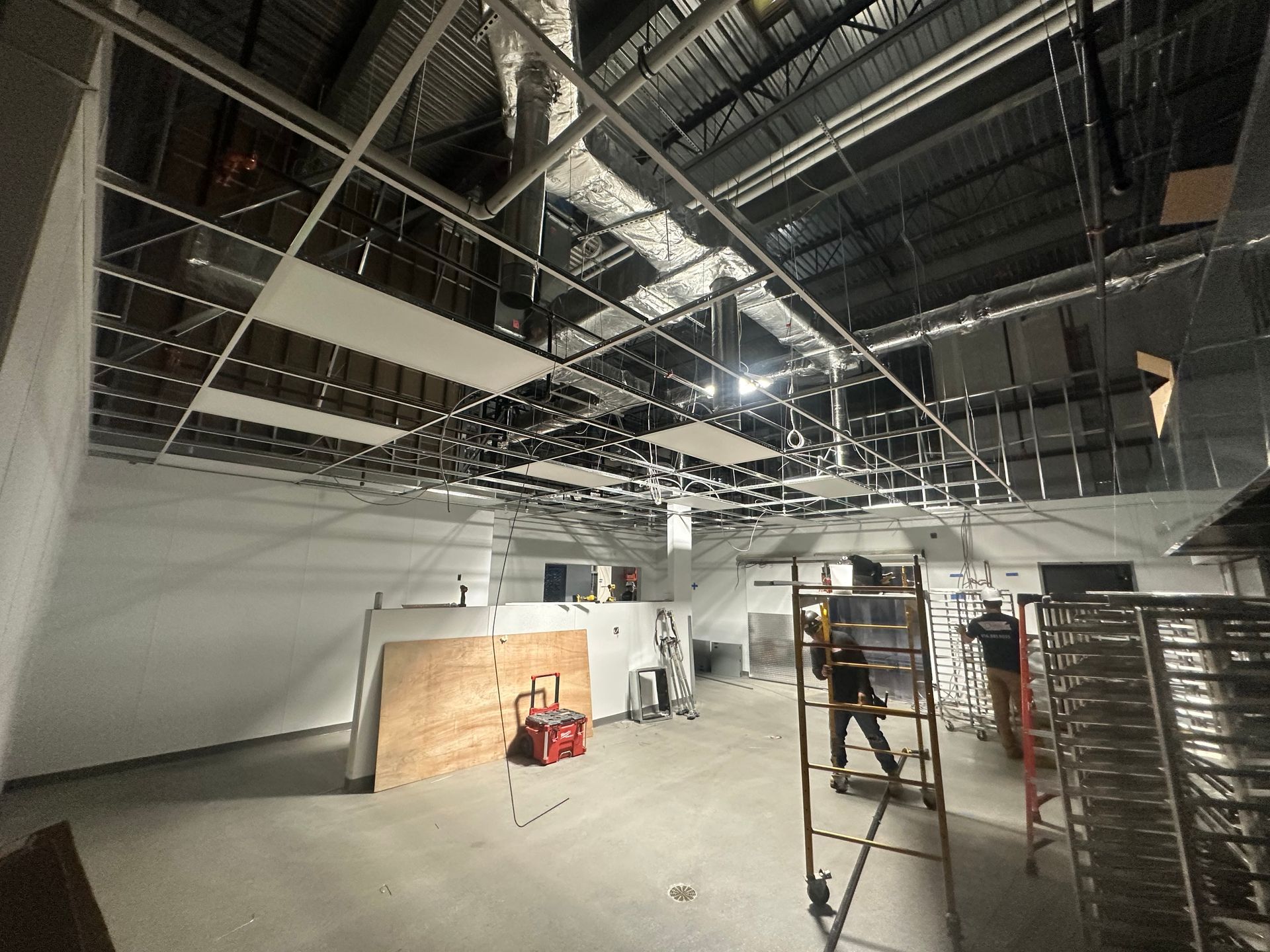 Construction site: Metal ceiling grid, unfinished walls, worker on a lift.