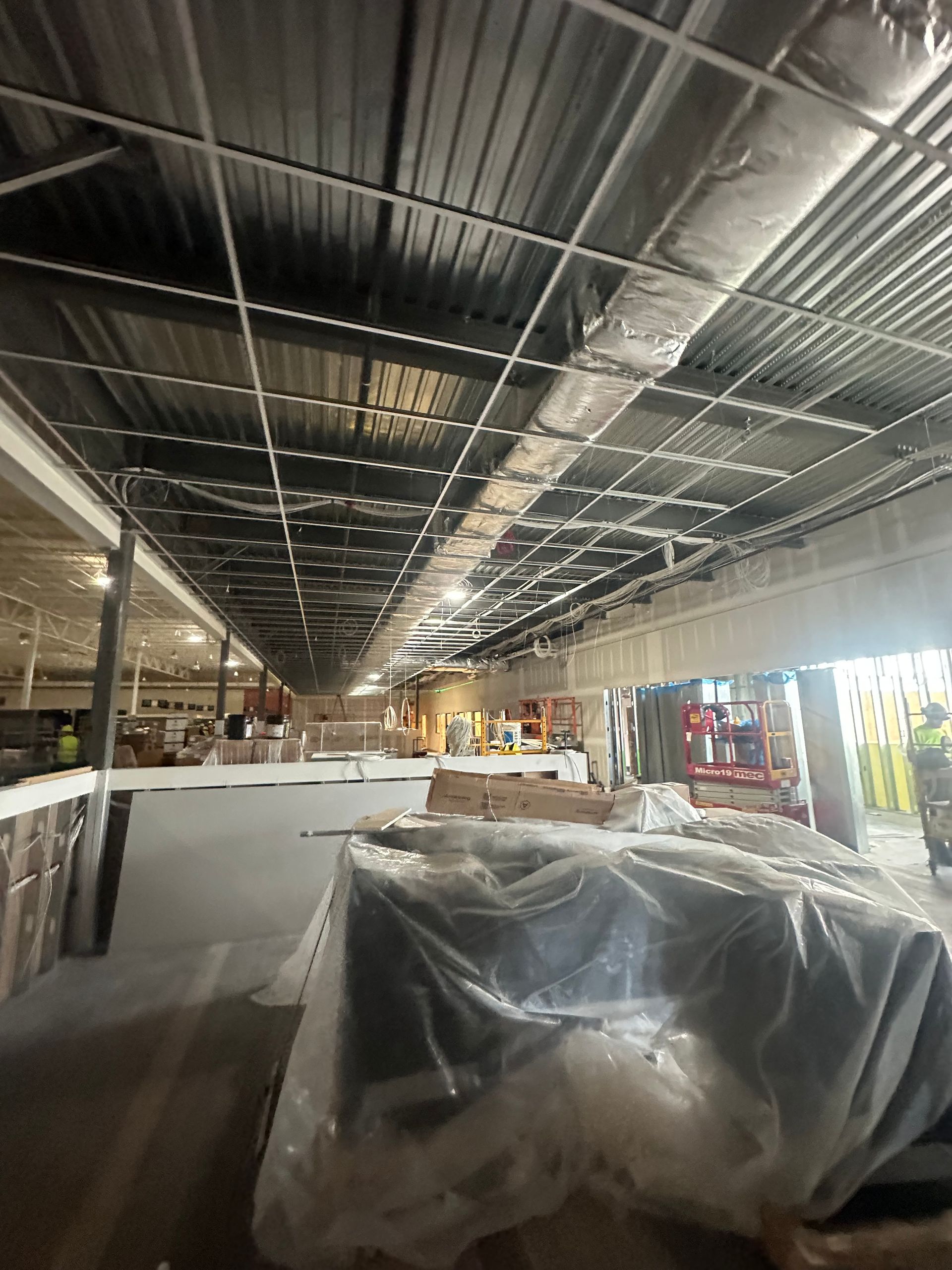 Interior of a commercial space under construction; metal framework, covered furniture, and exposed ceiling.