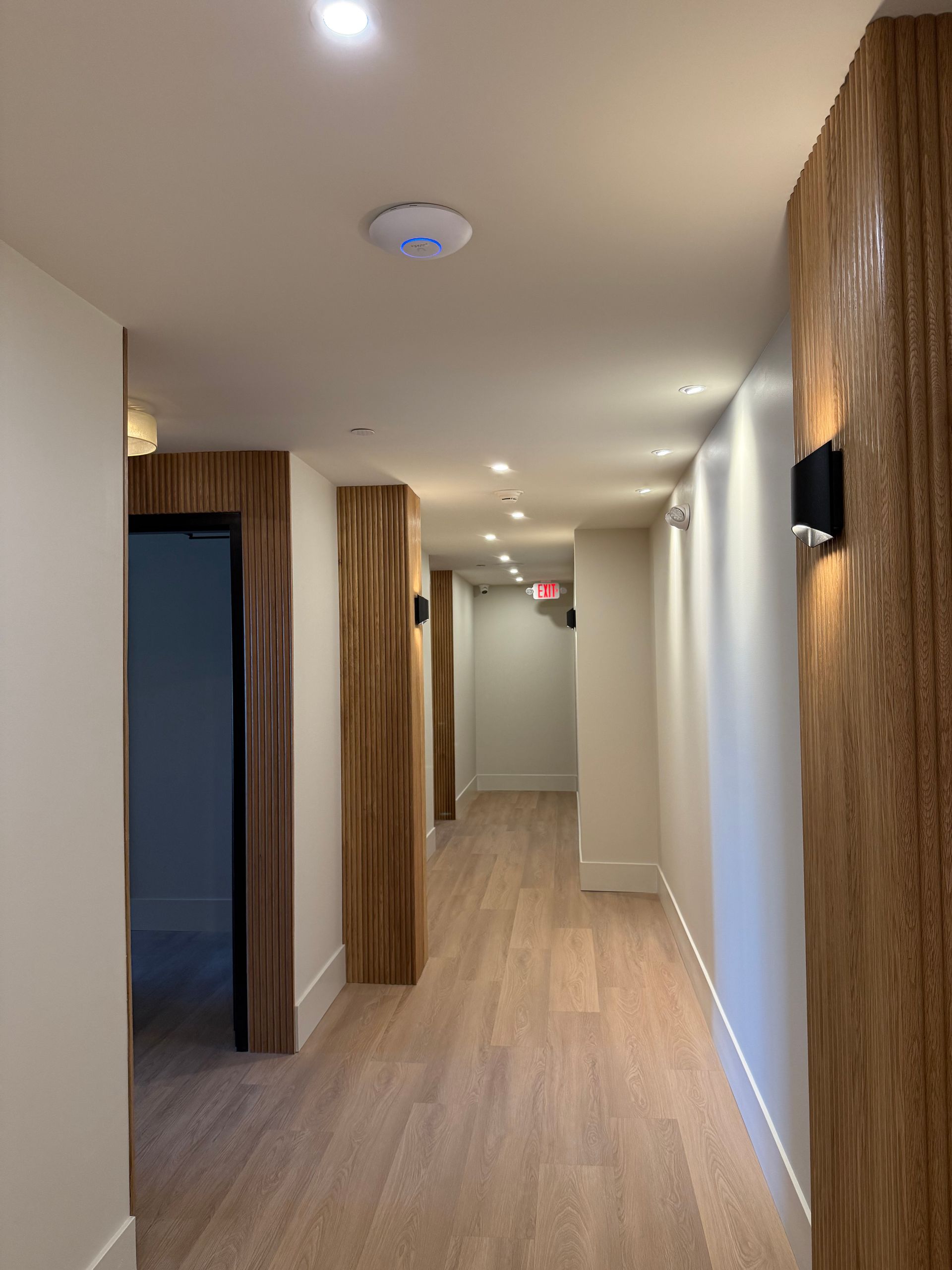Hallway with wood paneling, recessed lighting, and a light wooden floor.