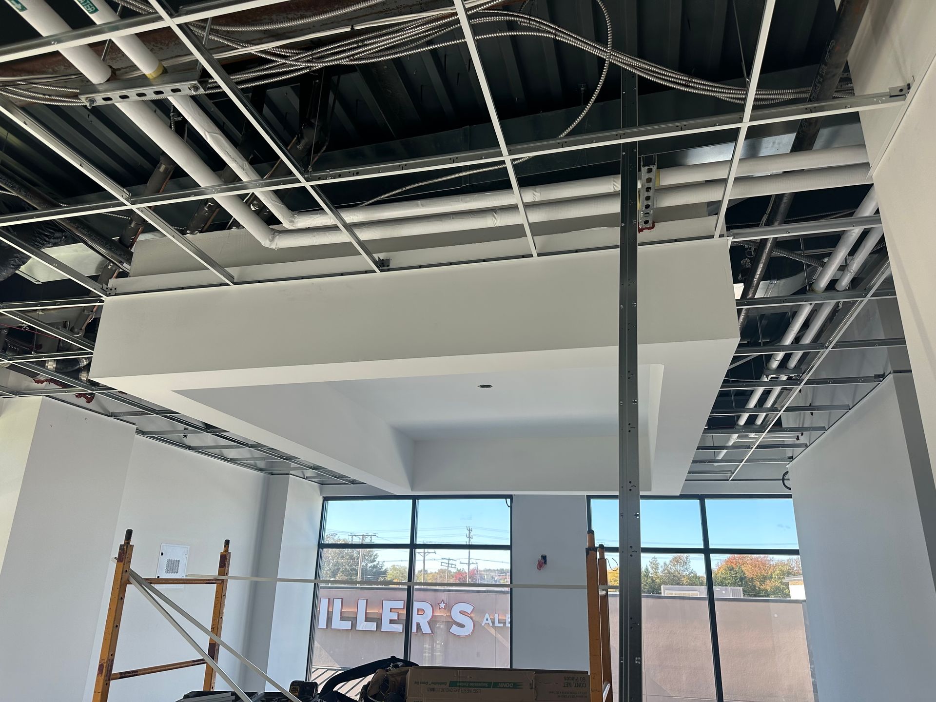 Construction site interior, unfinished ceiling with exposed beams, pipes, and a partially built soffit.