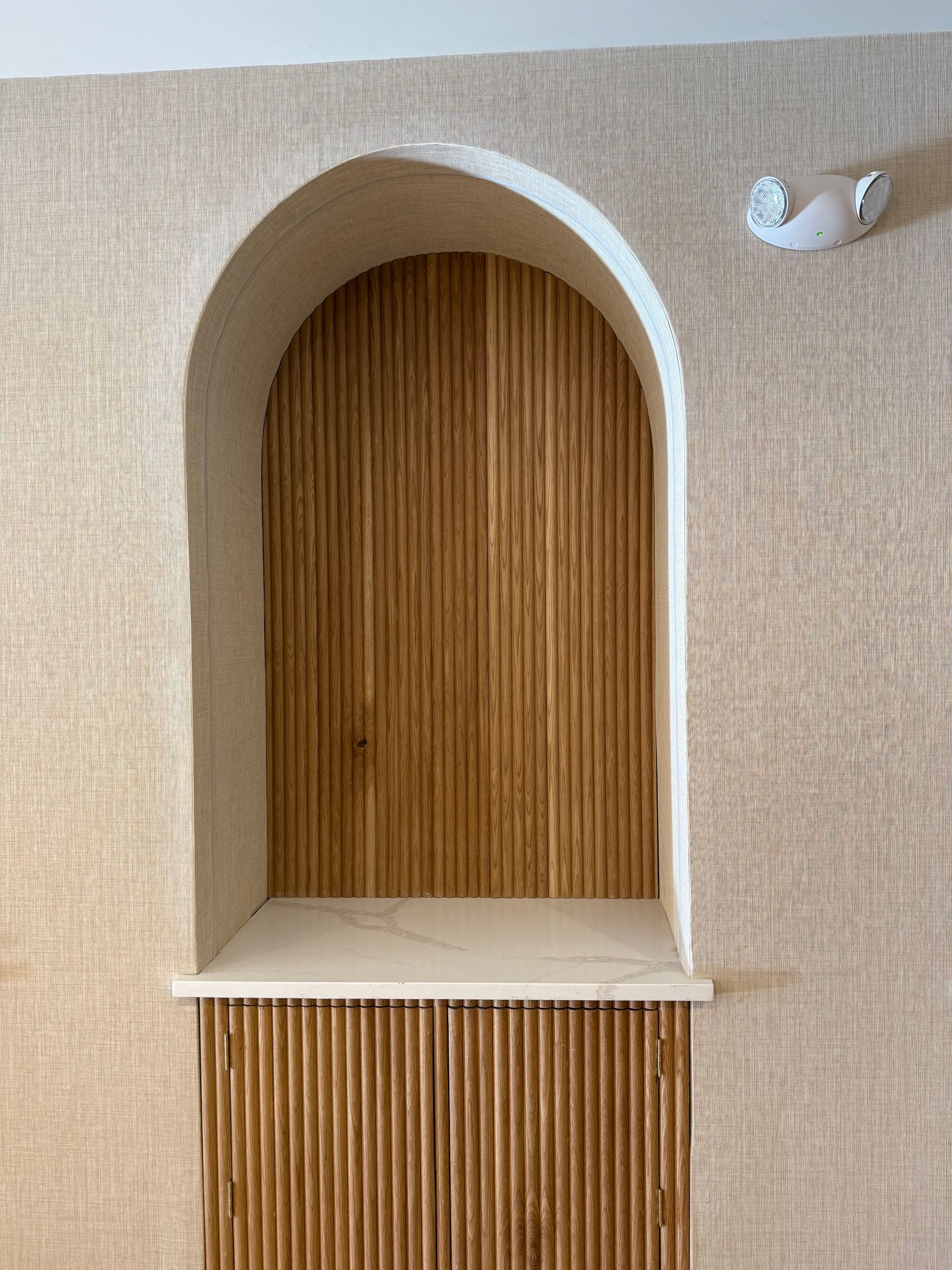 Arched niche with wooden interior and shelf, set in textured beige wall. A small seal sculpture is visible.