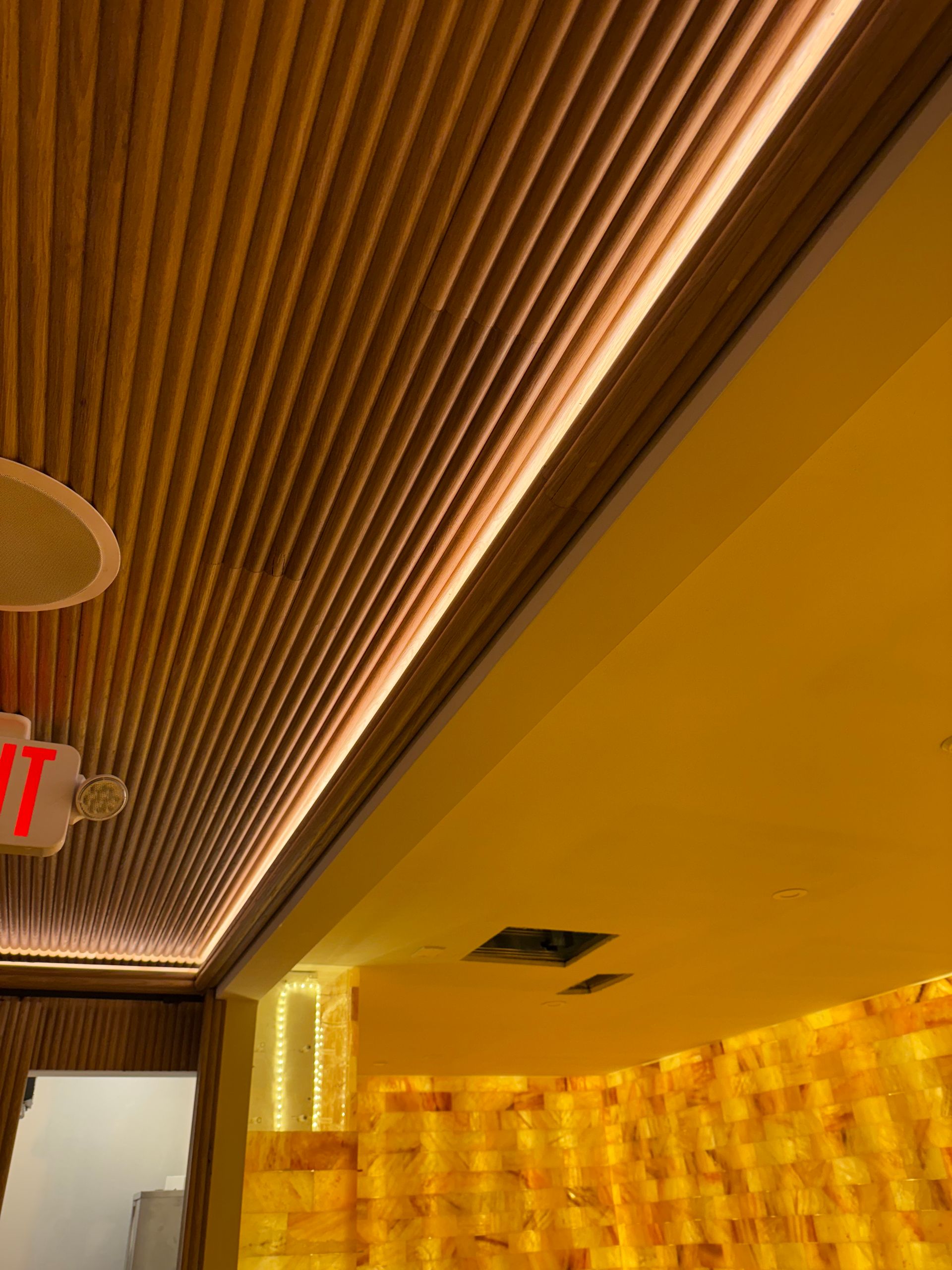 Wooden slatted ceiling with recessed lighting. A yellow wall with a salt brick wall.