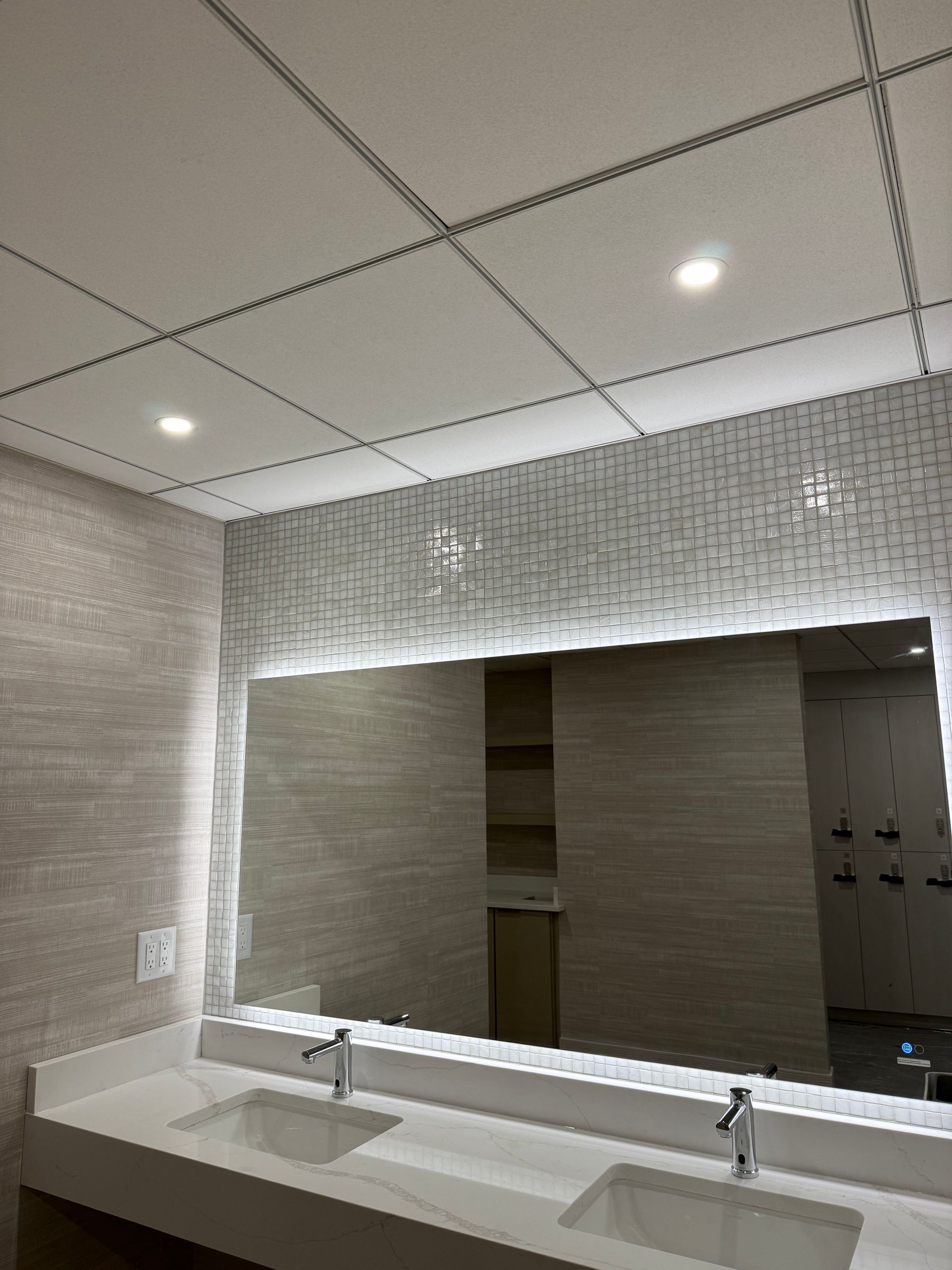 Bathroom with a large mirror, two sinks, and a textured wall with overhead lighting.
