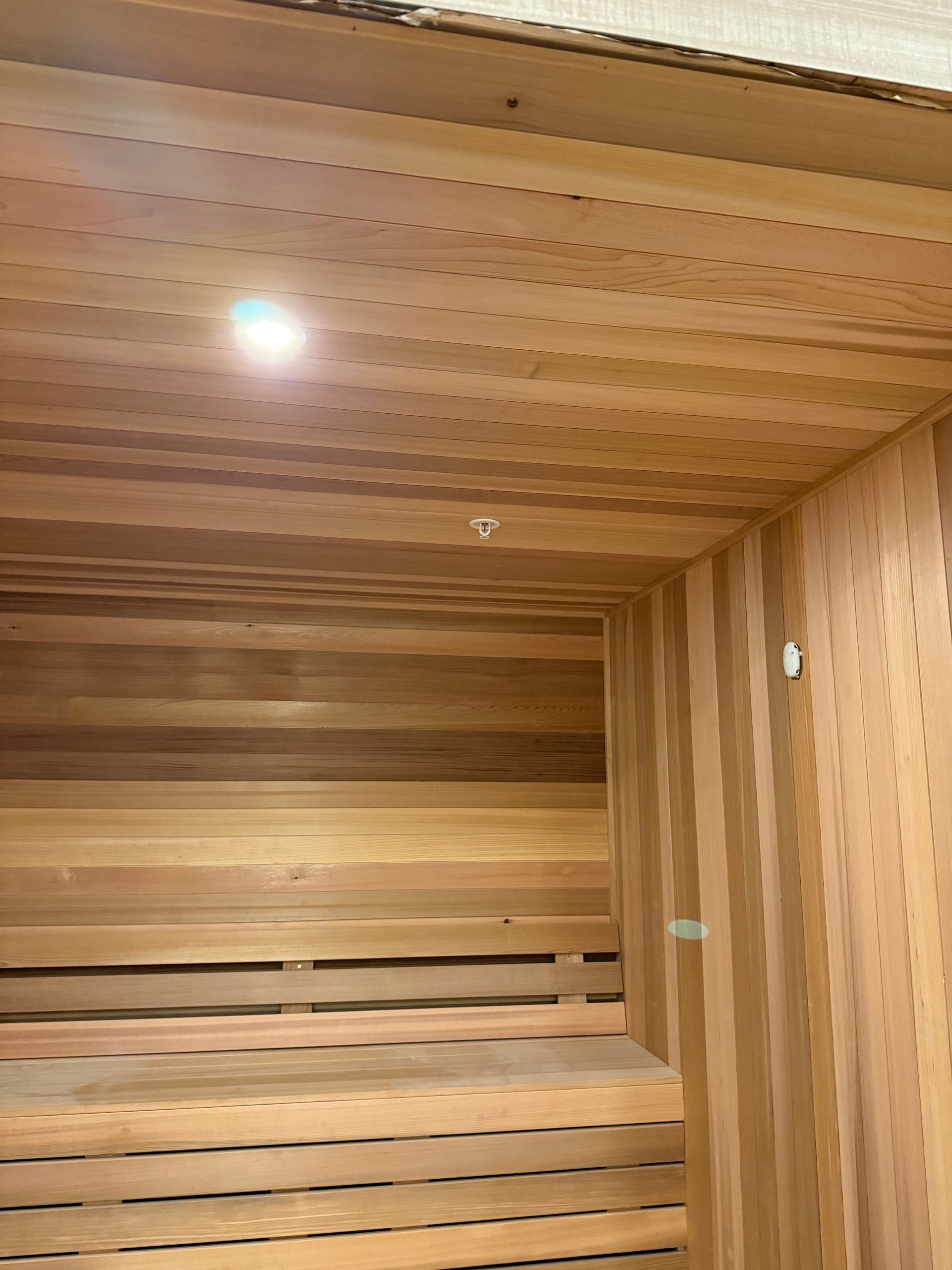 Wooden sauna interior with horizontal and vertical planks. Bench and ceiling light visible.