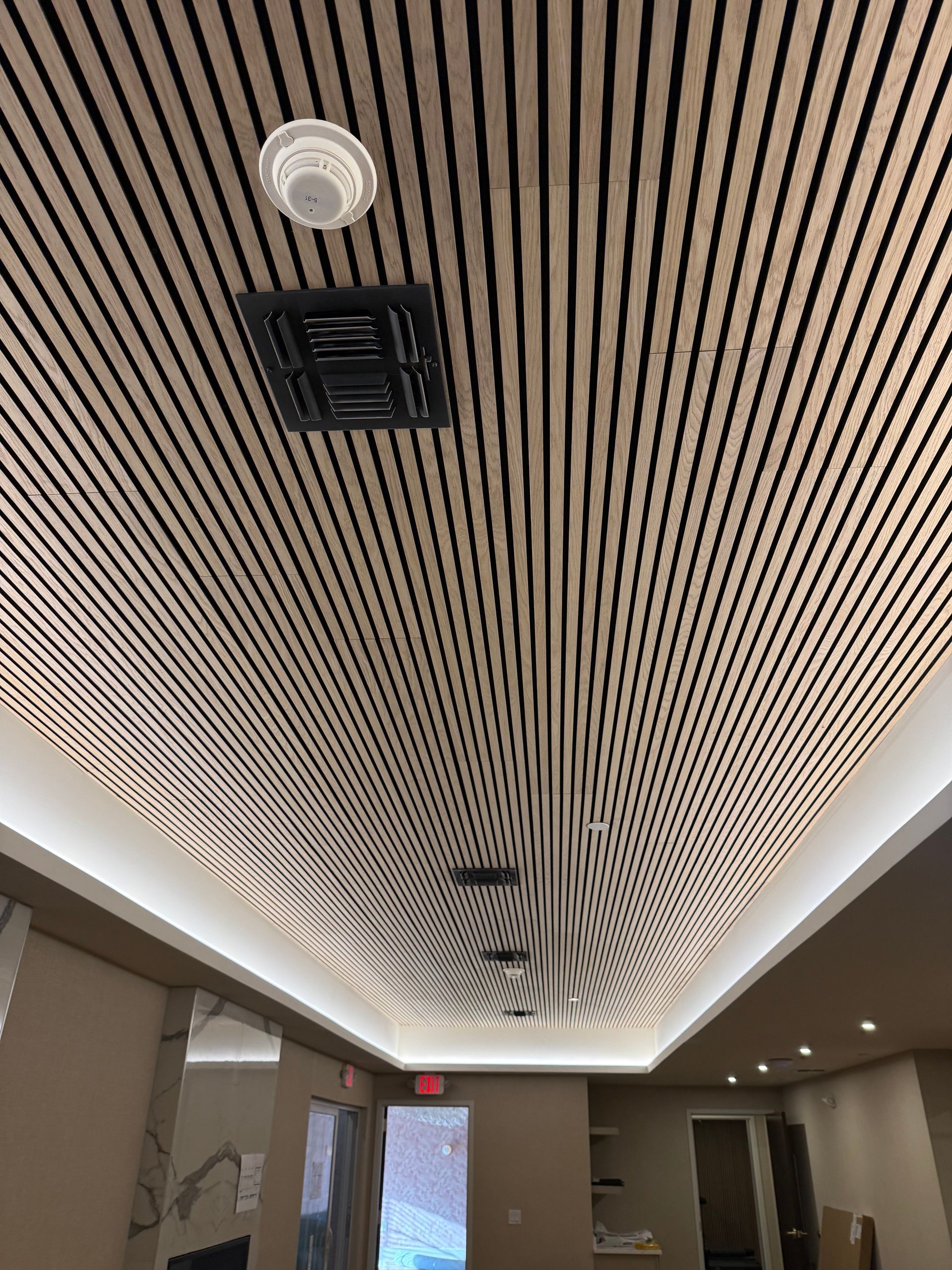 Beige and black slatted ceiling with recessed lighting and air vent. Interior view.