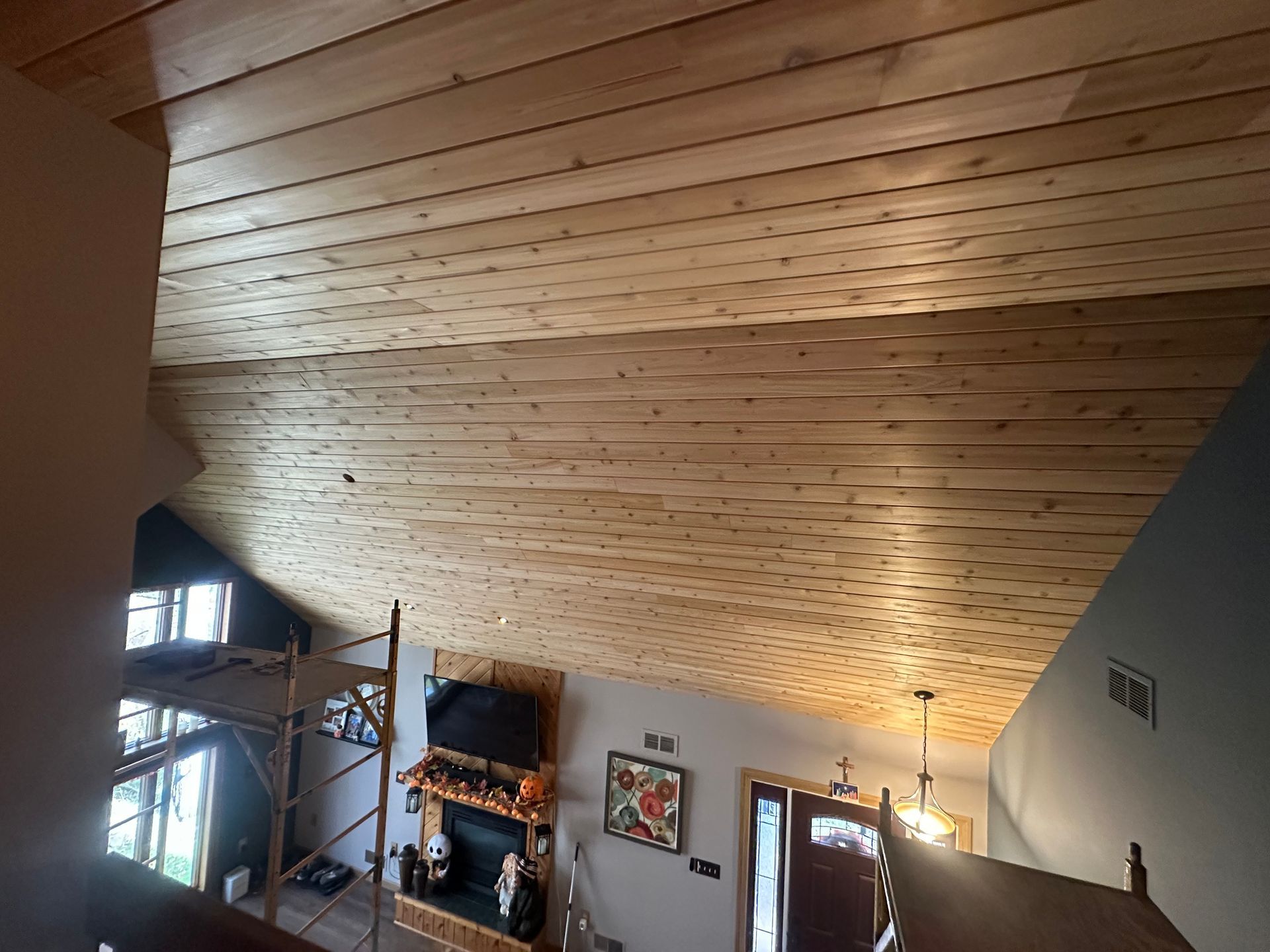 Wooden plank ceiling in a home with a fireplace, TV, and large windows.