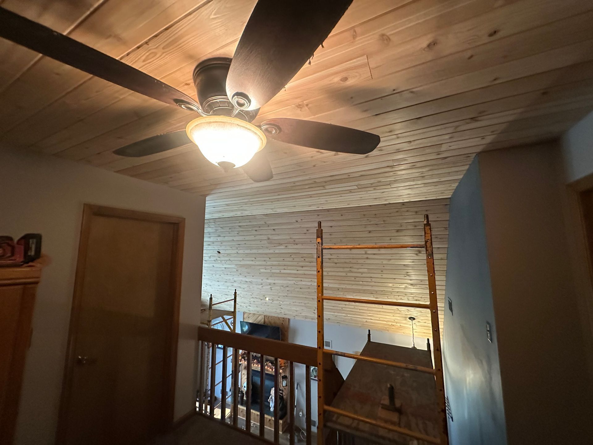 Ceiling fan on a wood-paneled ceiling. A ladder leans against the wall in the loft.