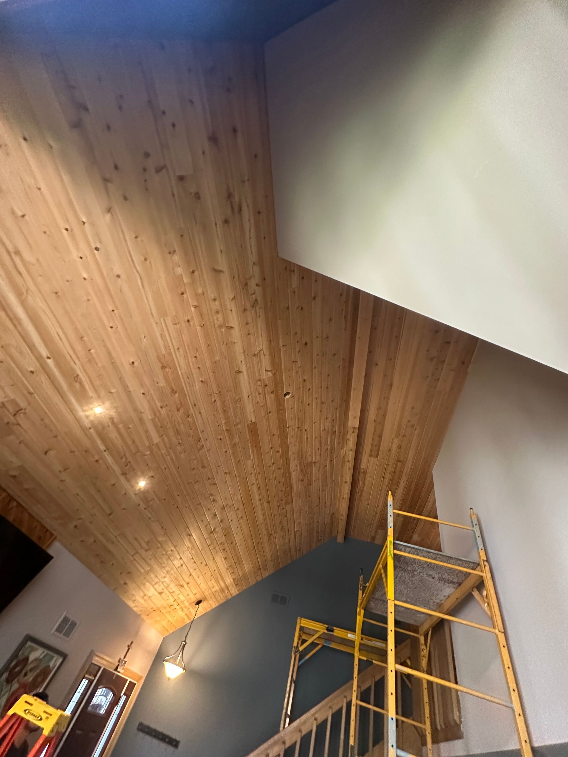 Wooden plank ceiling in a room with a scaffolding. Light beige walls and natural wood ceiling.