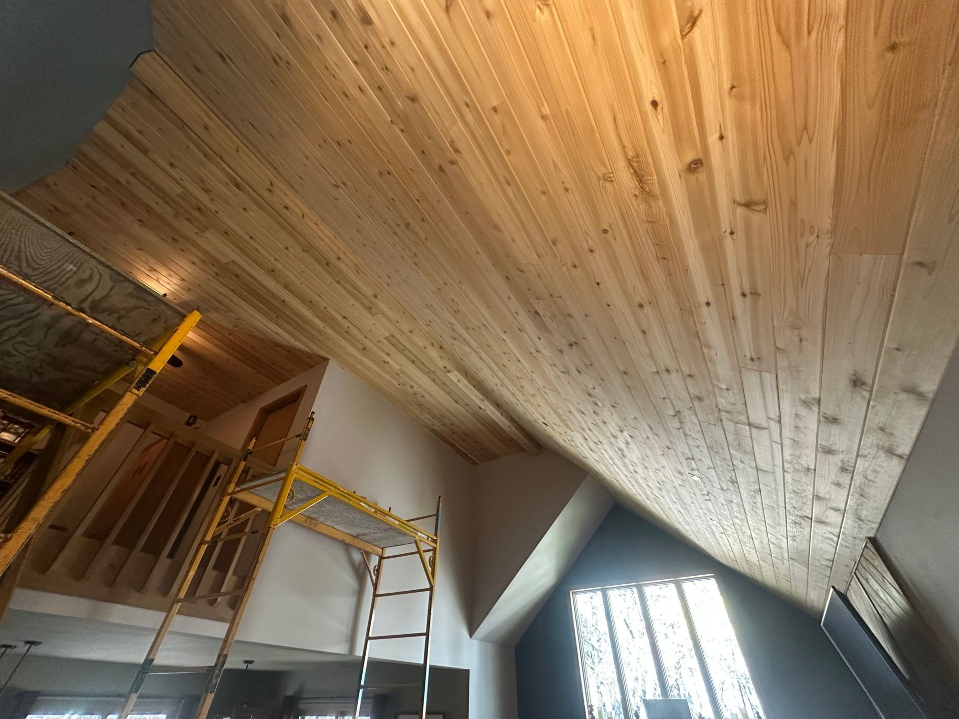 Wooden ceiling construction in a room, with scaffolding and an angled window.