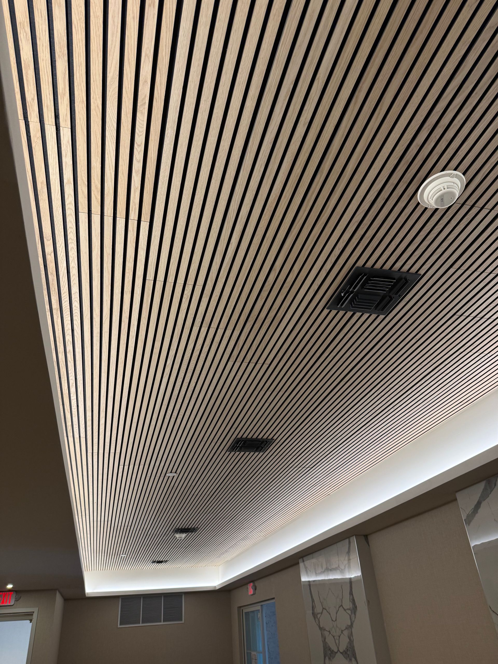 Ceiling with curving wood and black striped pattern, recessed lighting, and a smoke detector.