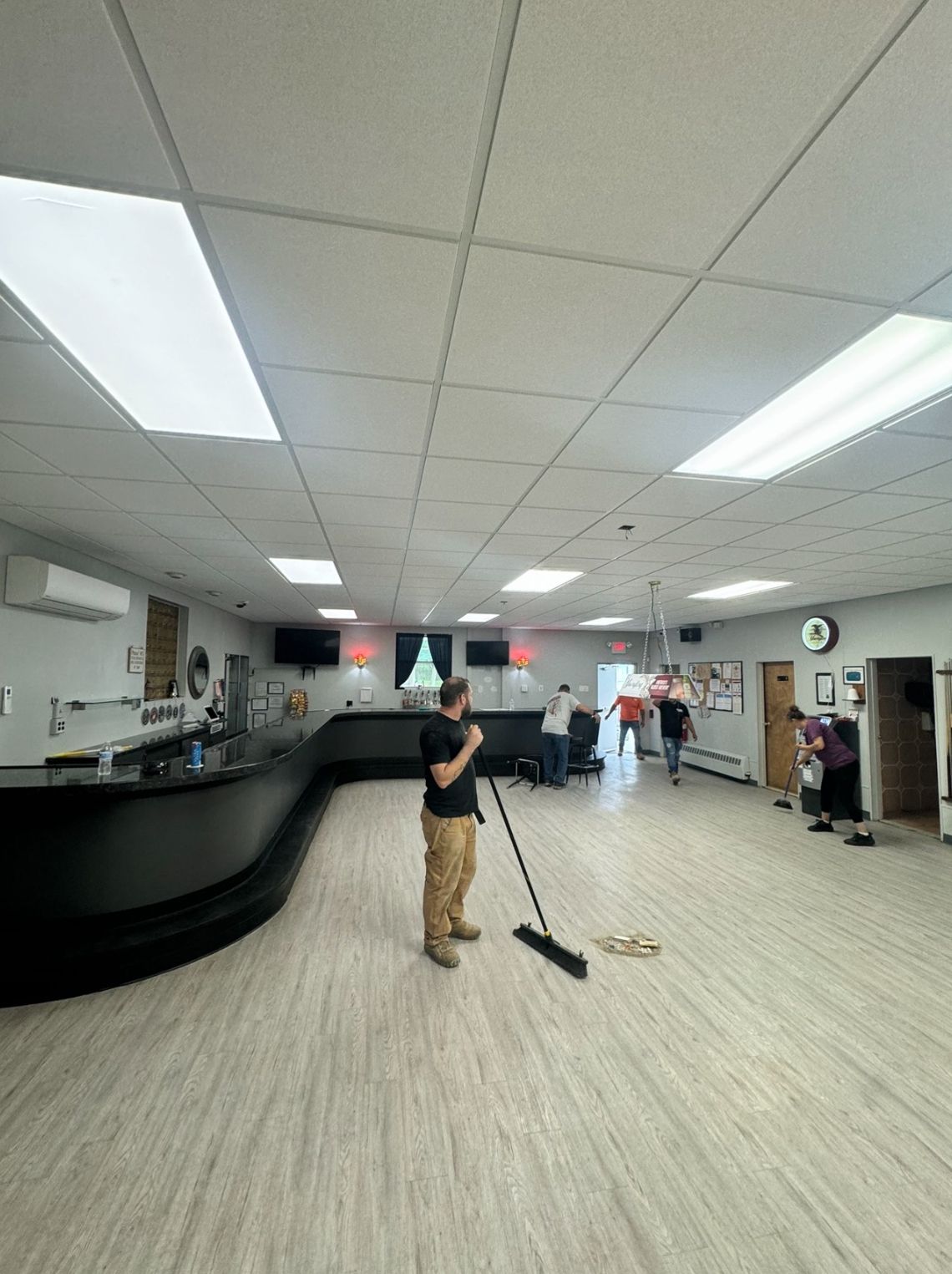 A person sweeping a large room with a long black bar and people in the background.