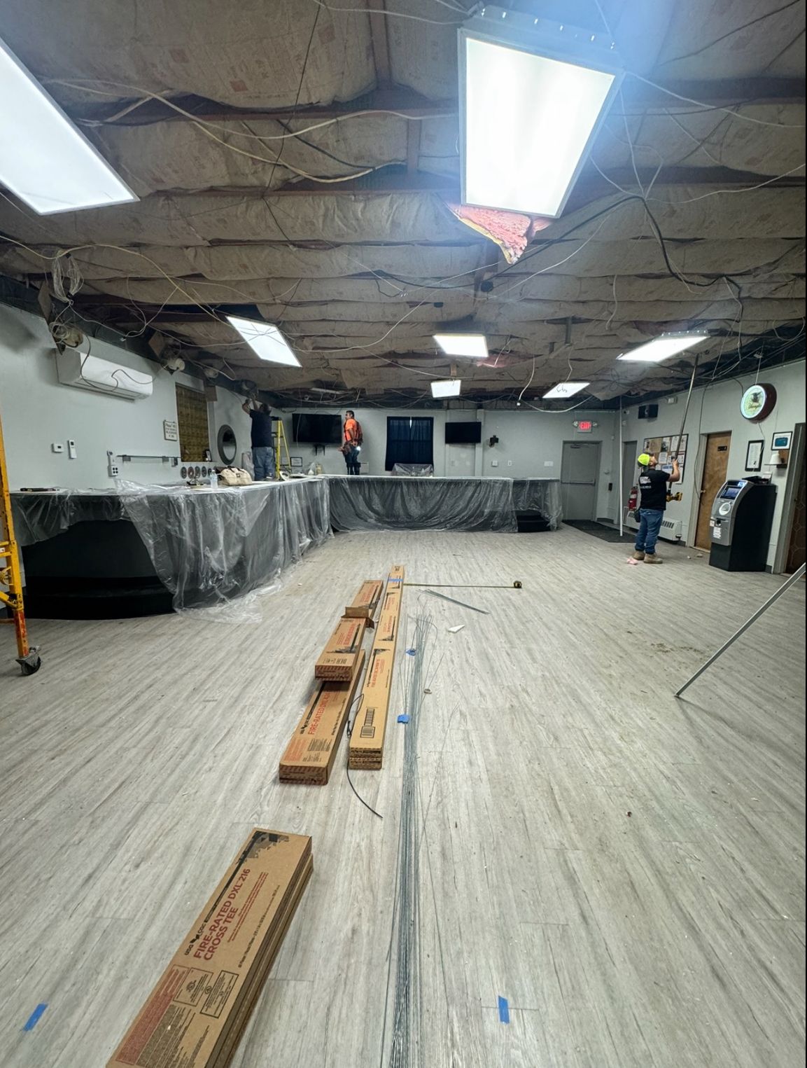 Workers are present, the ceiling and floor have damage, and construction materials are visible.