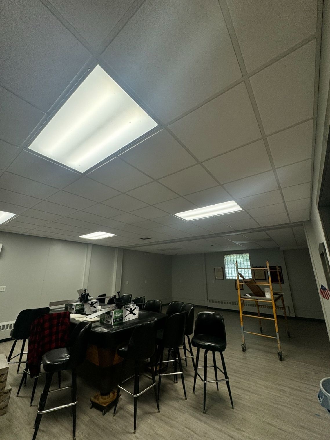 Interior of a room with a bar, stools, and overhead lighting. A ladder sits in the background near a window.