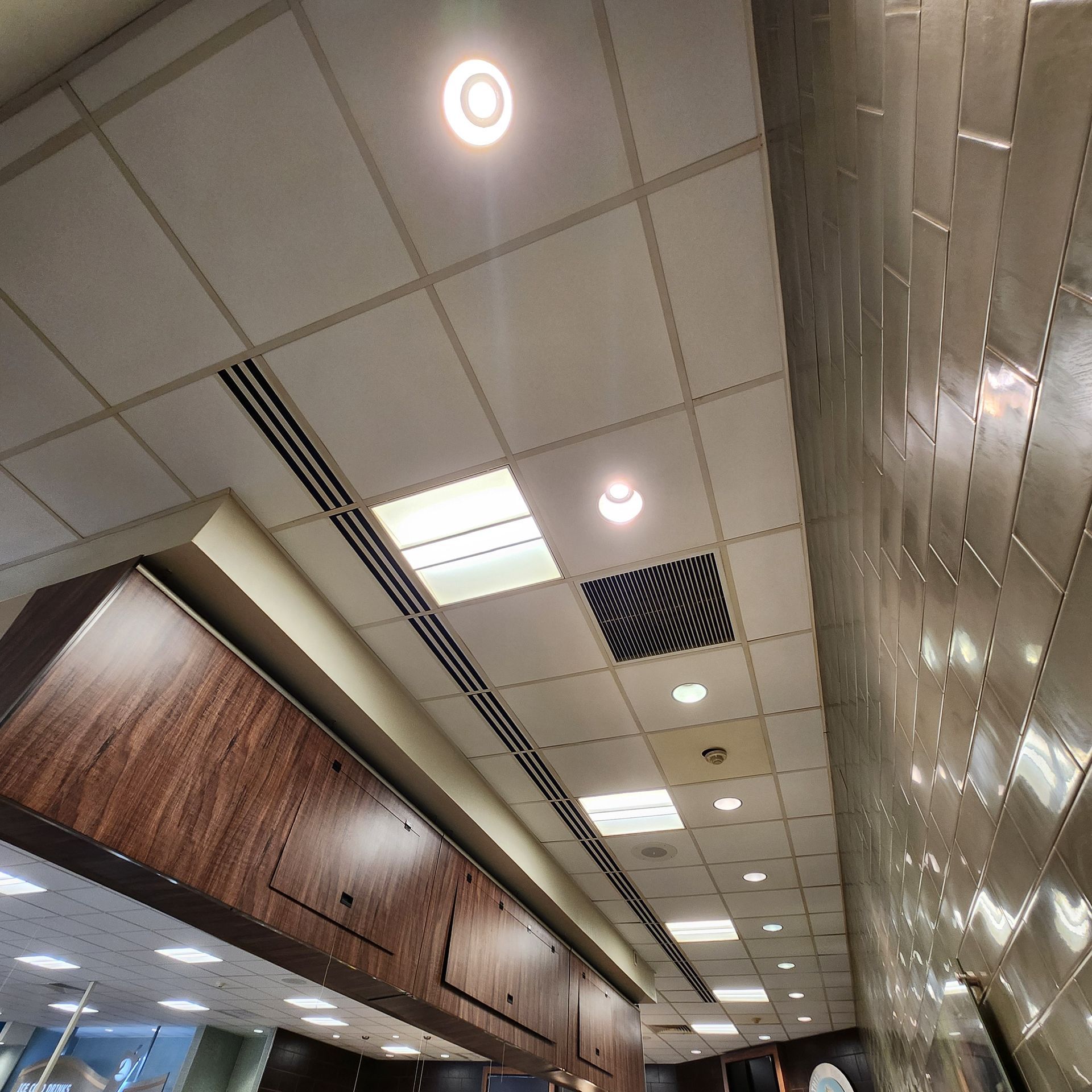 A ceiling with recessed lights, vents, and a decorative wall with metal tiles.