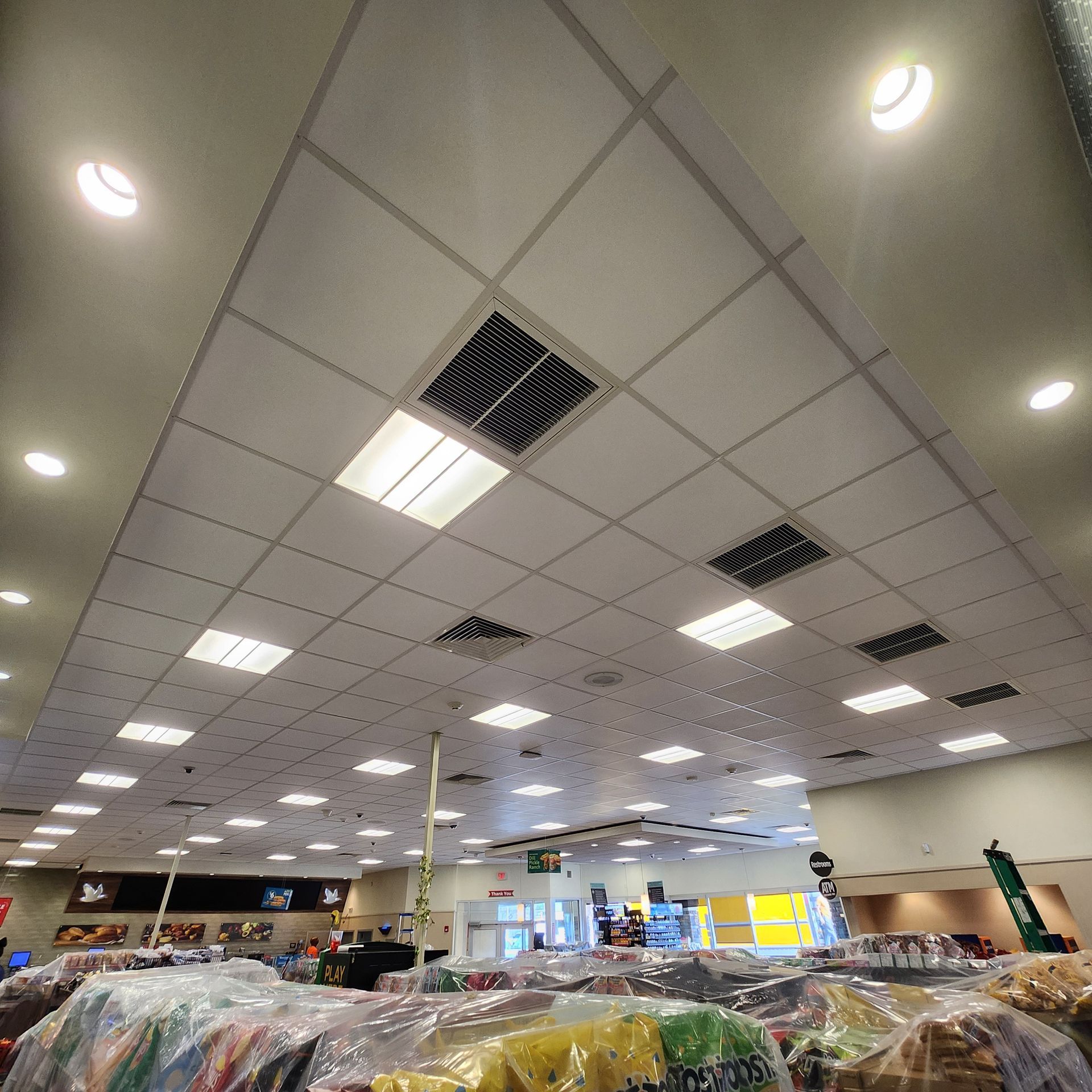Looking up at a tiled ceiling with lights, vents, and a store interior visible below.