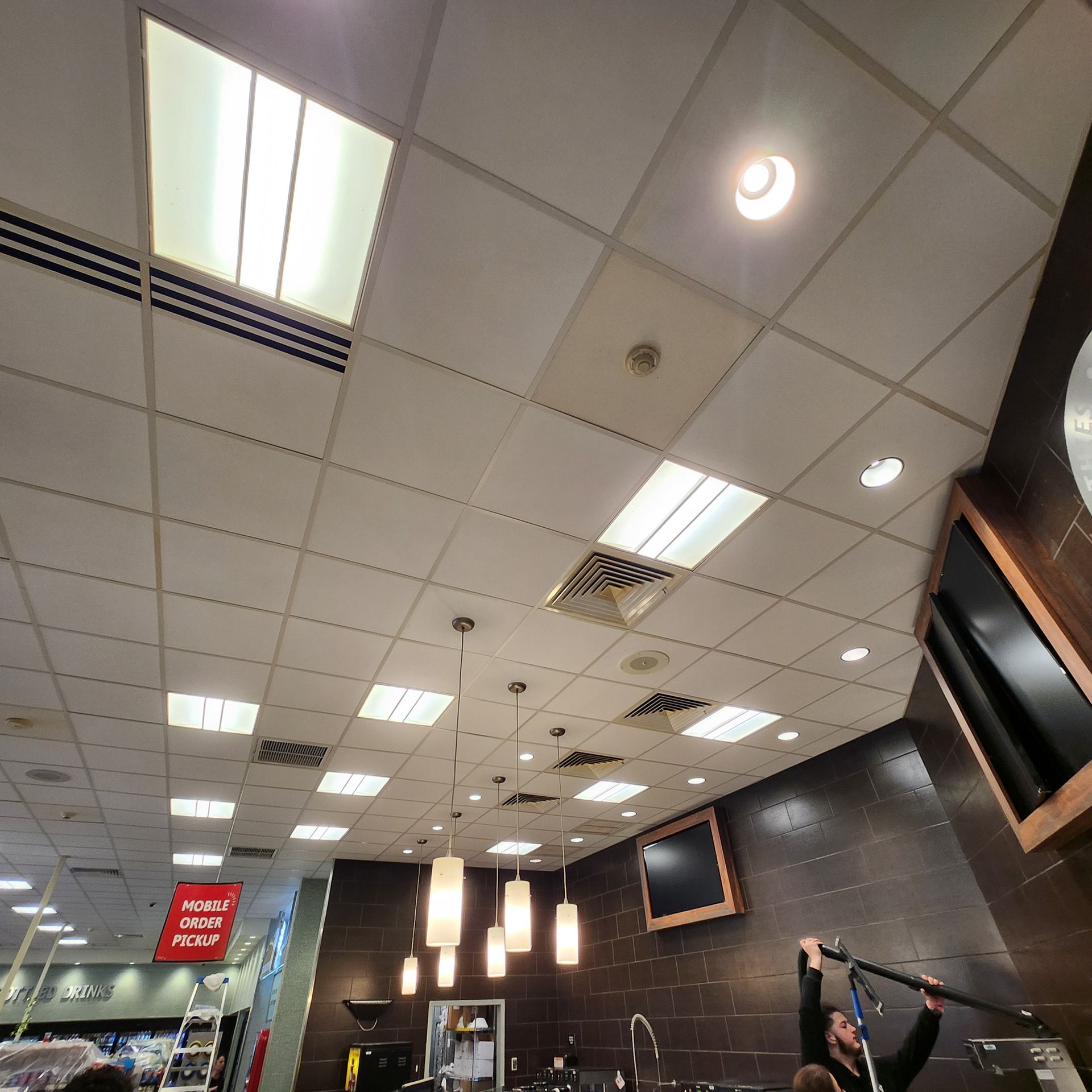Ceiling tiles with recessed lighting, small bar area with hanging pendant lights and a person holding a boom mic.