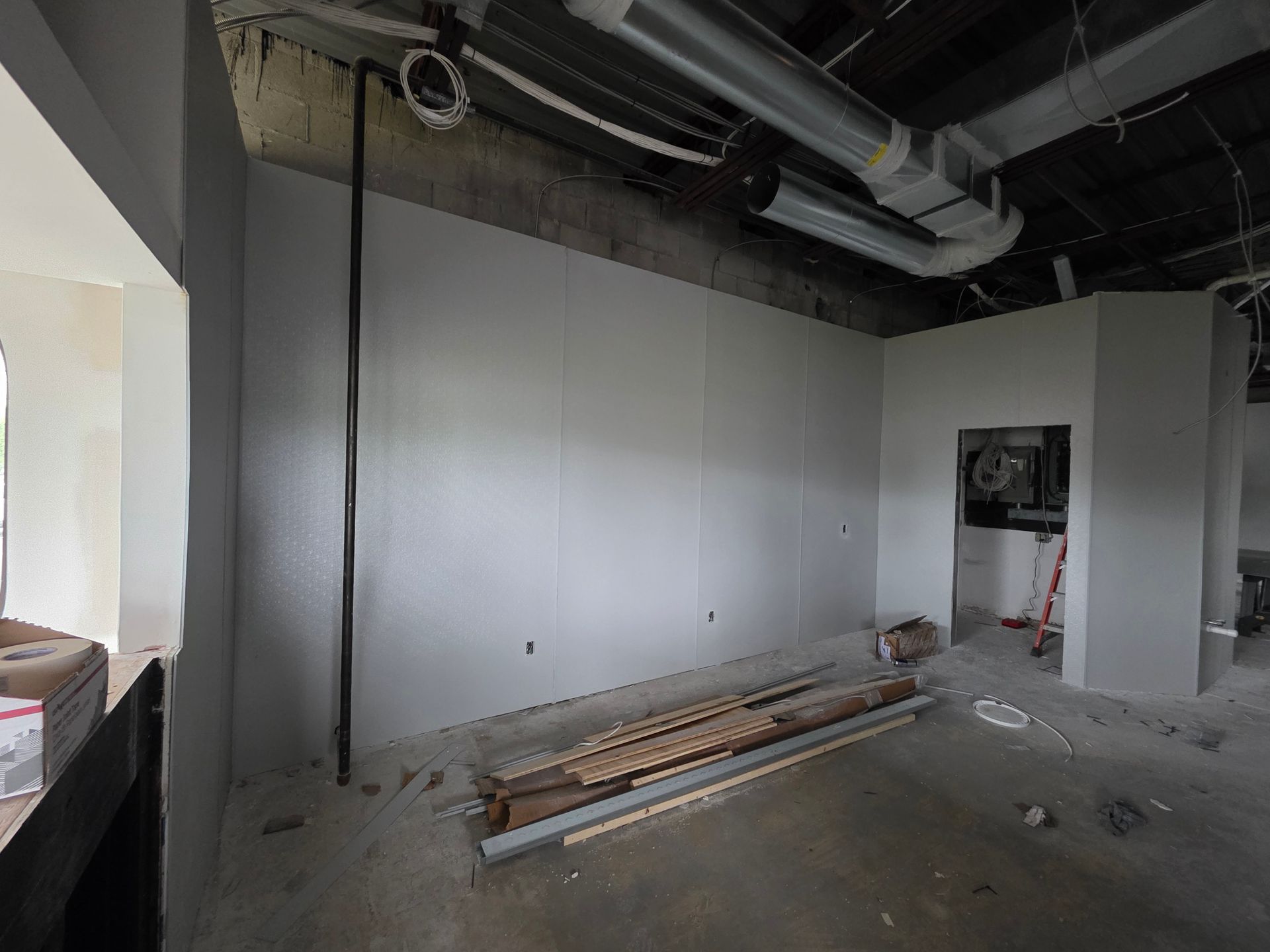 Interior room under construction, with painted walls, concrete floor, exposed pipes, and materials.