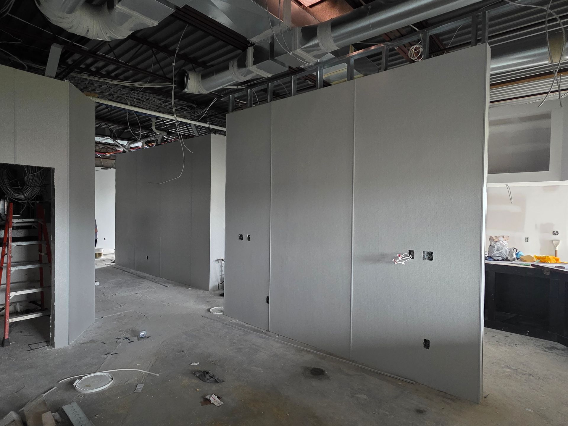 Interior construction: Gray drywall walls, exposed ceiling, unfinished space. Electrical outlets visible.