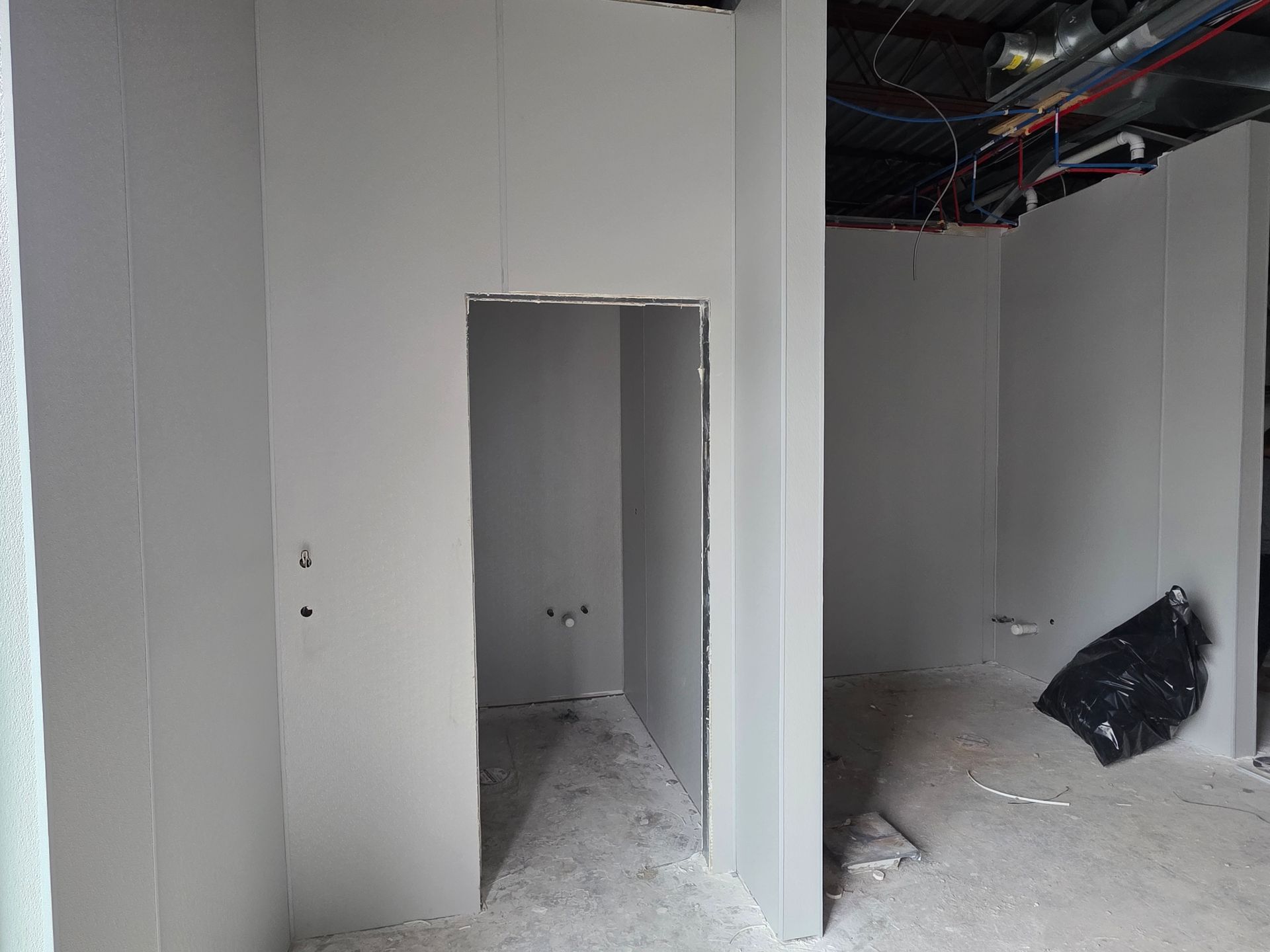 Interior of a room under construction with gray drywall walls and an open doorway.