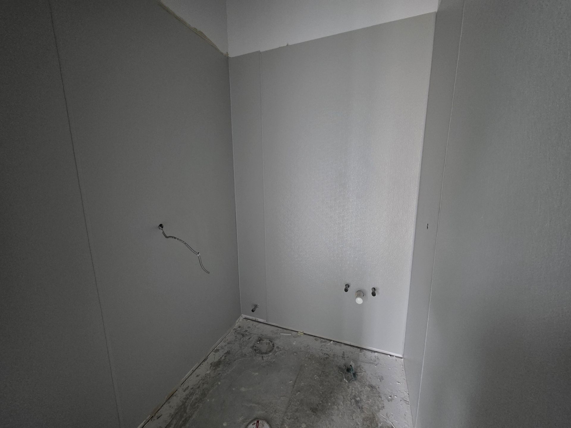 Empty room with gray walls and a concrete floor, possibly a bathroom under construction.