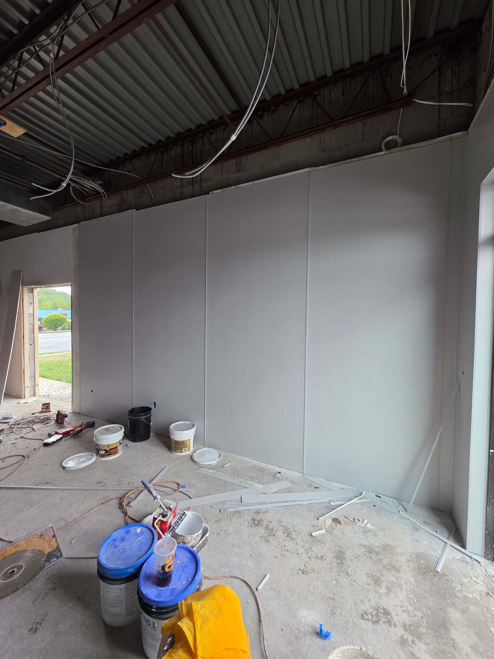Interior room under construction, with painted wall panels. Buckets and tools on concrete floor.