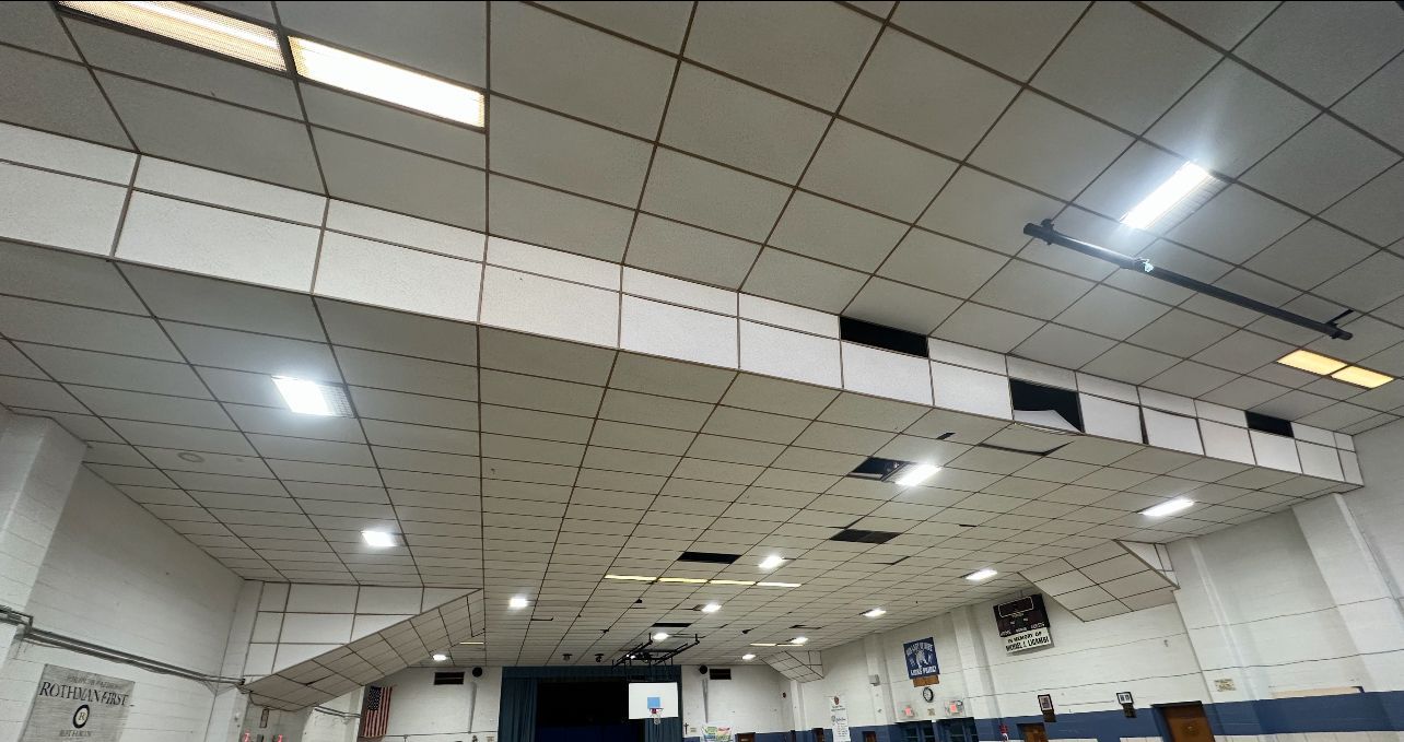Gymnasium ceiling with white grid panels, recessed lights, and visible ductwork.