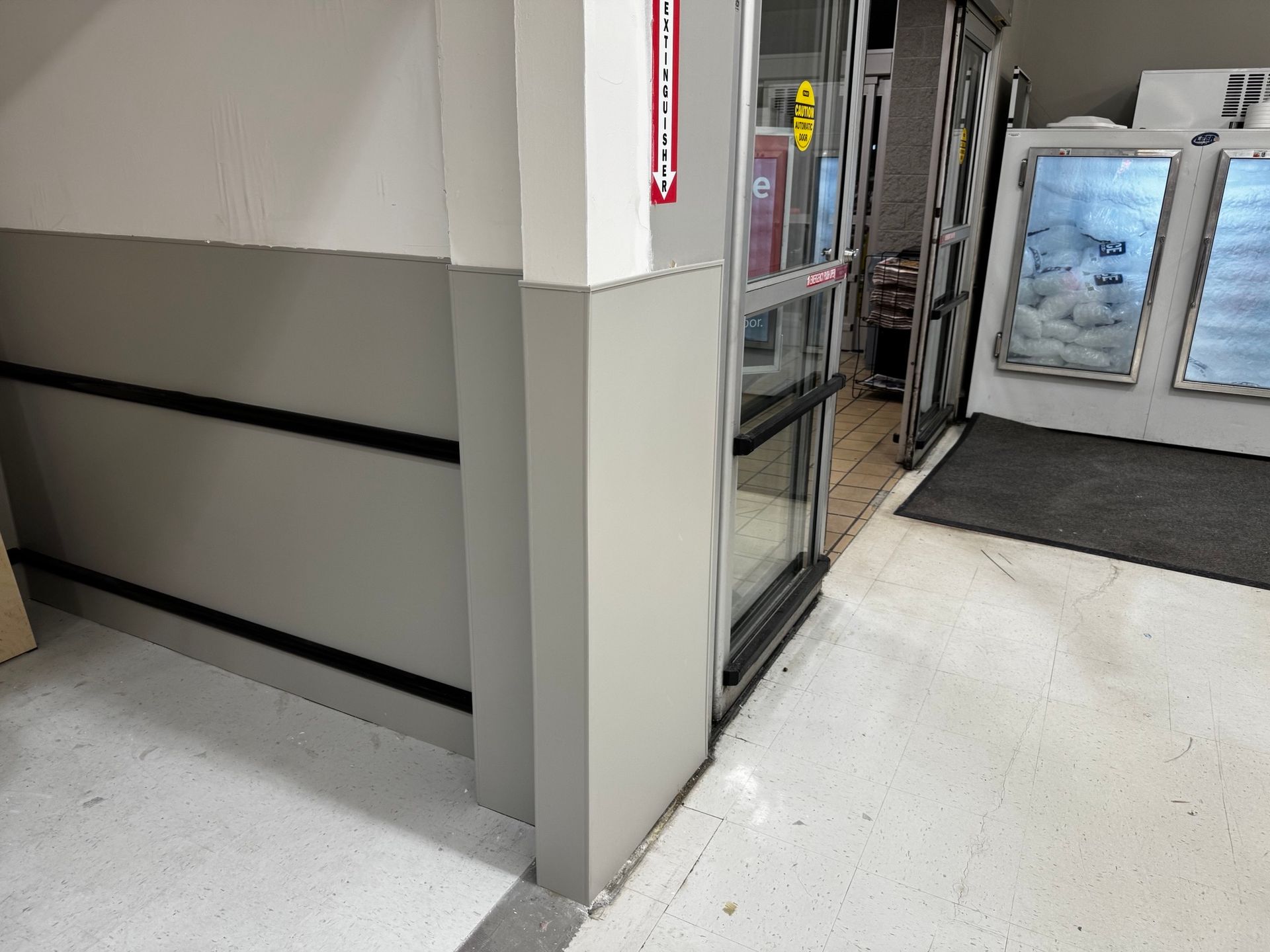 Entrance with a glass door, light gray walls, and black bumper guards.