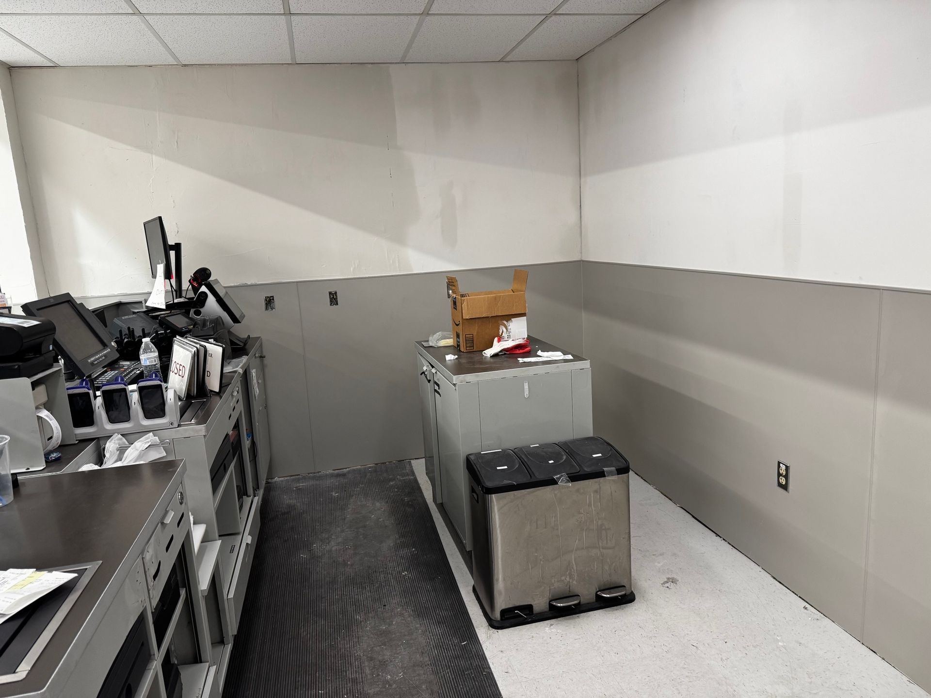 A commercial kitchen corner with gray and white panel walls, a stainless steel counter, and a trash can.