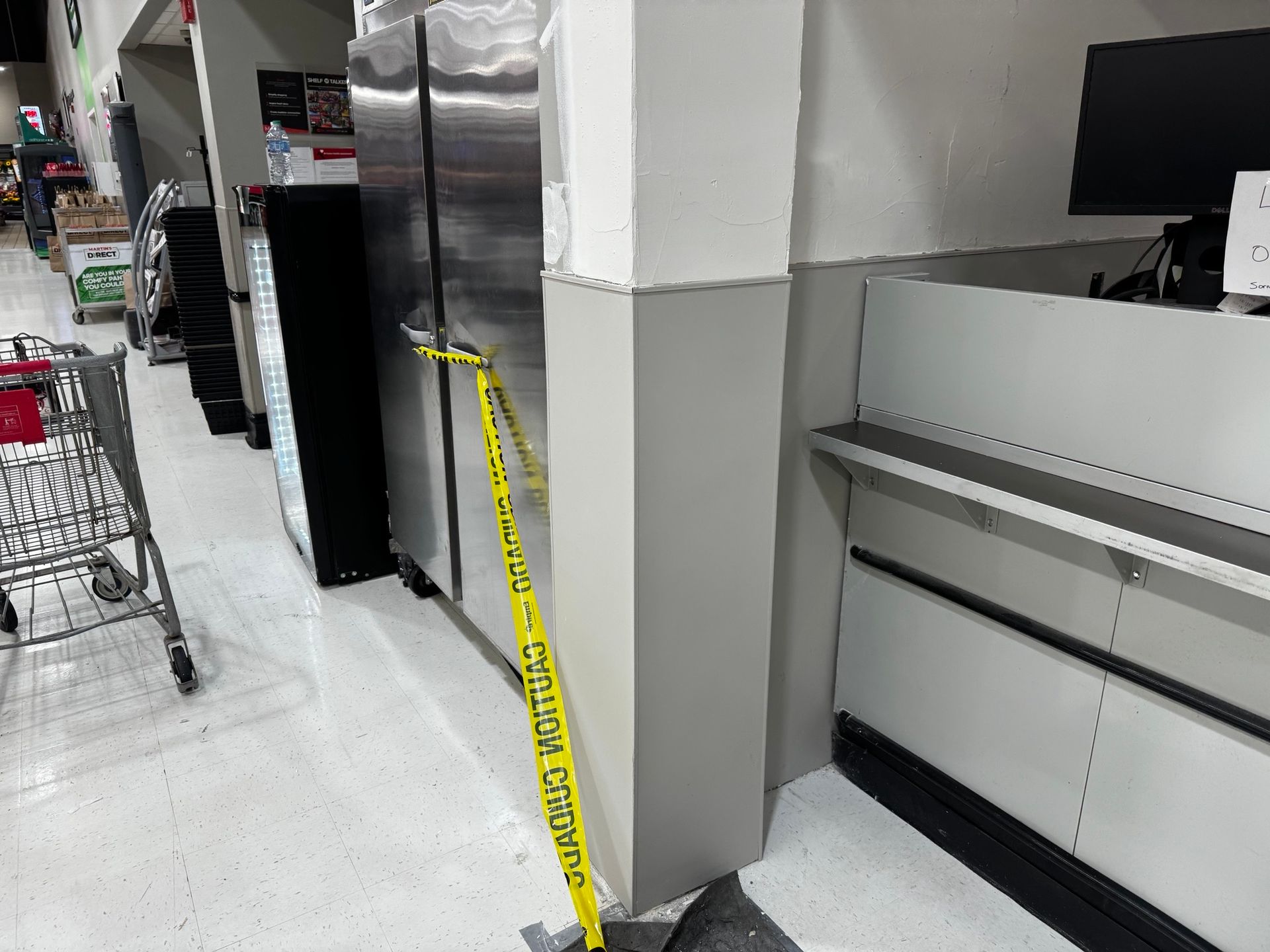 Grocery store interior with a refrigerator sectioned off with caution tape near a checkout counter.