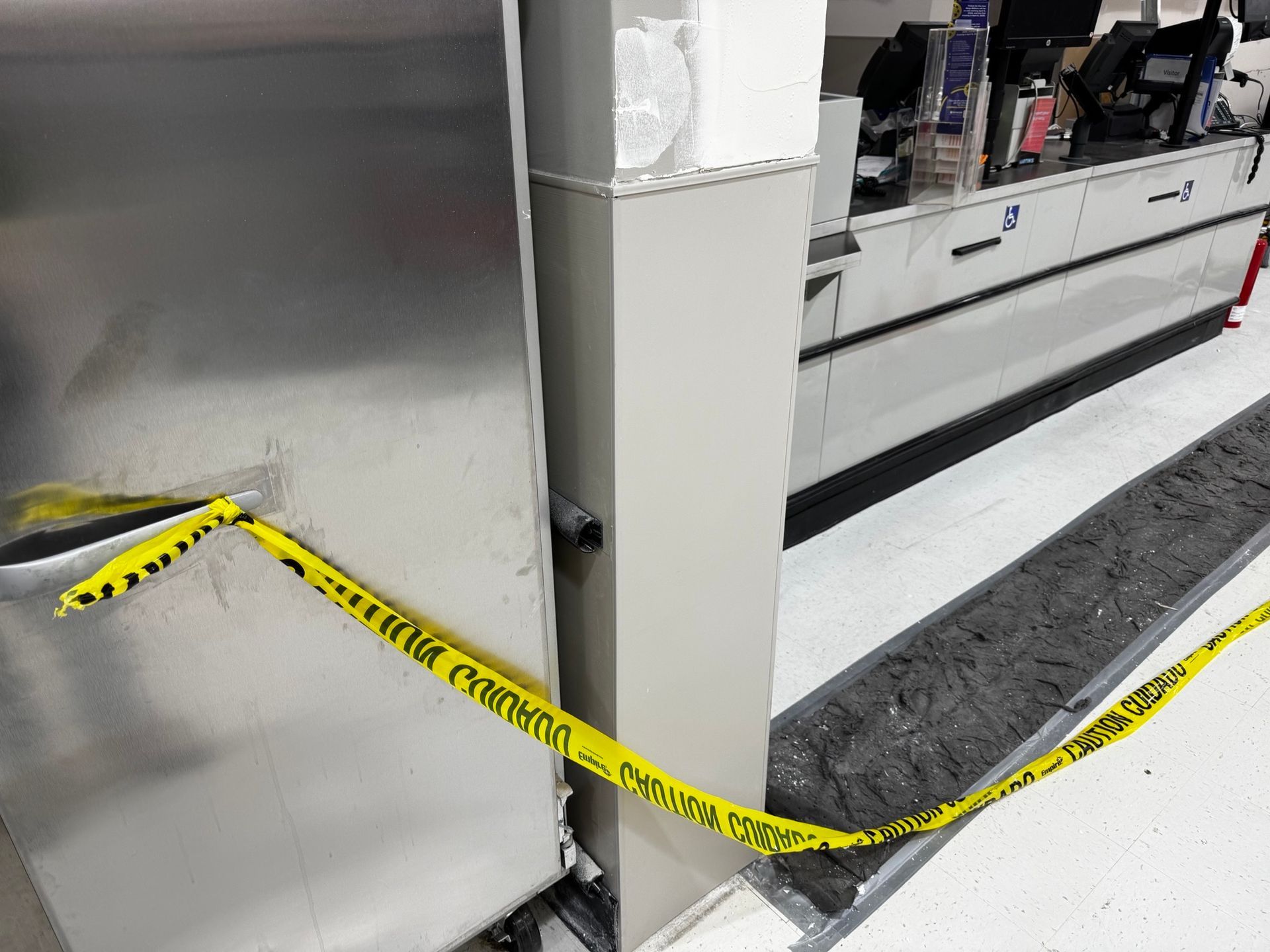 Yellow caution tape surrounds a damaged metal structure, near a store checkout counter.