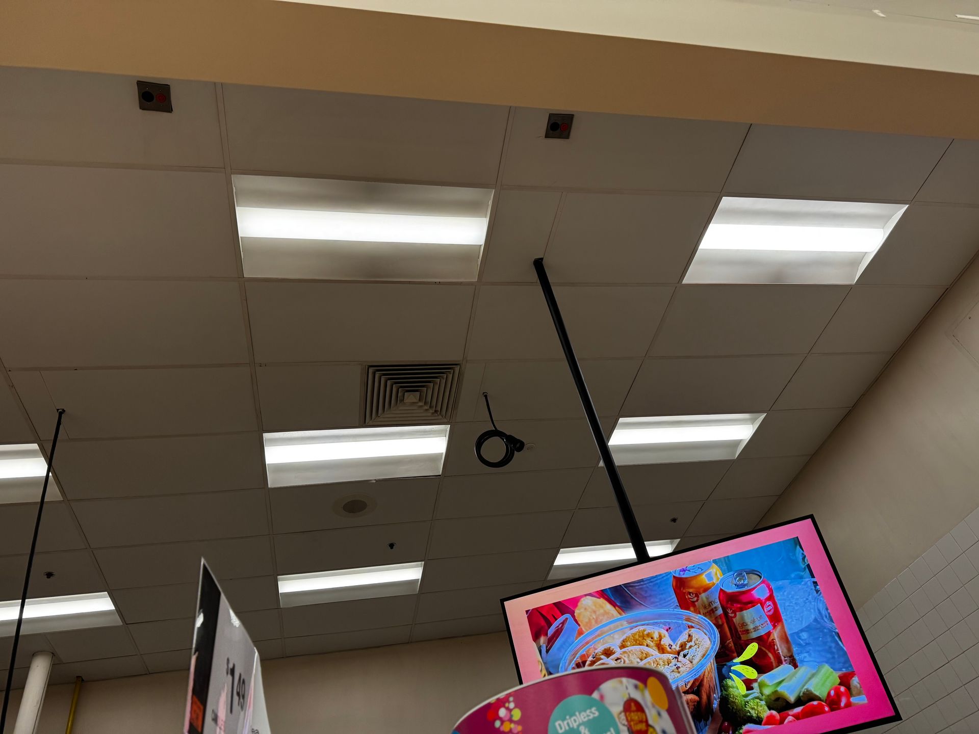 Ceiling with square fluorescent lights, a hanging sign with food, and a sign.