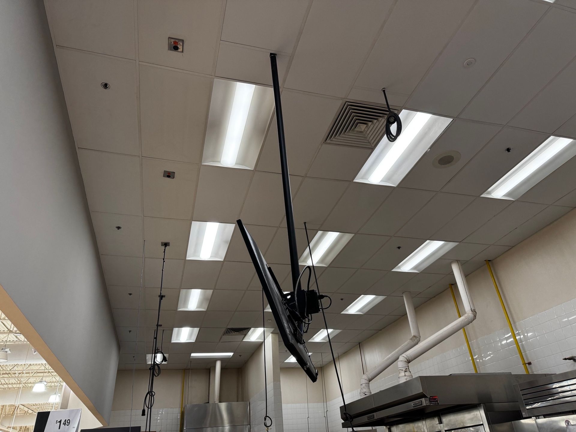 A ceiling-mounted monitor hangs above a commercial kitchen. Bright fluorescent lights illuminate the space.