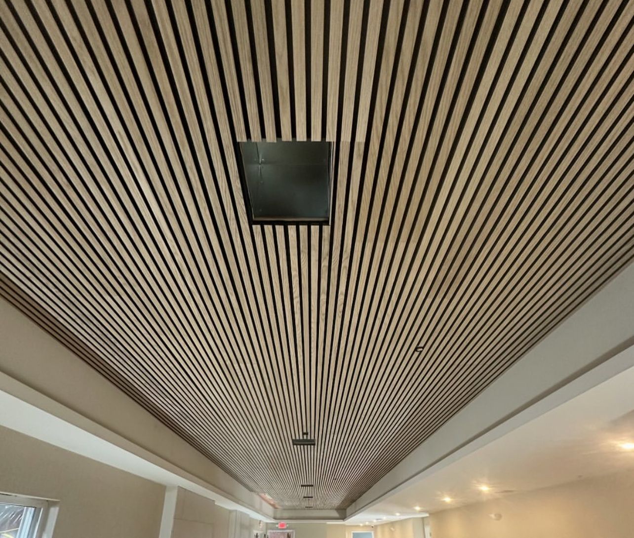 Slatted wooden ceiling with black lines, recessed black square, and lights in a room.