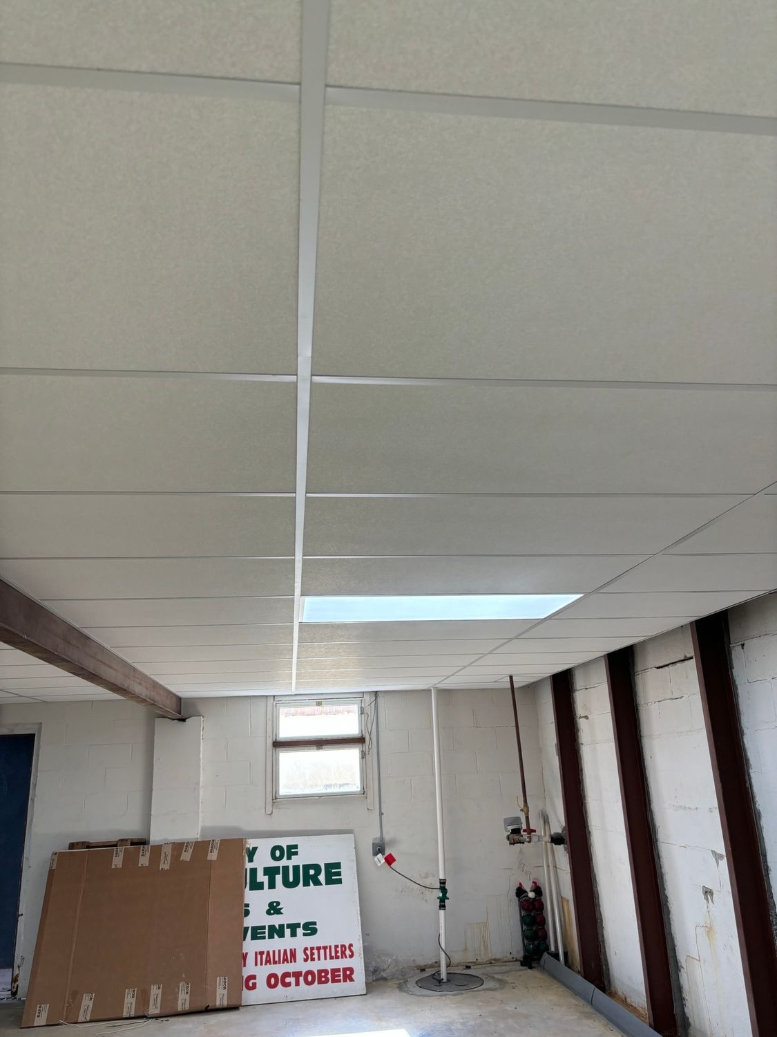 Low-angle view of a ceiling with suspended tiles and exposed support beams in a room with partial walls.