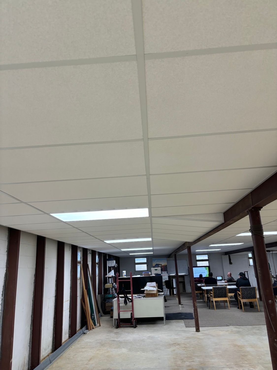 Office interior with a drop ceiling, fluorescent lights, and several people working.