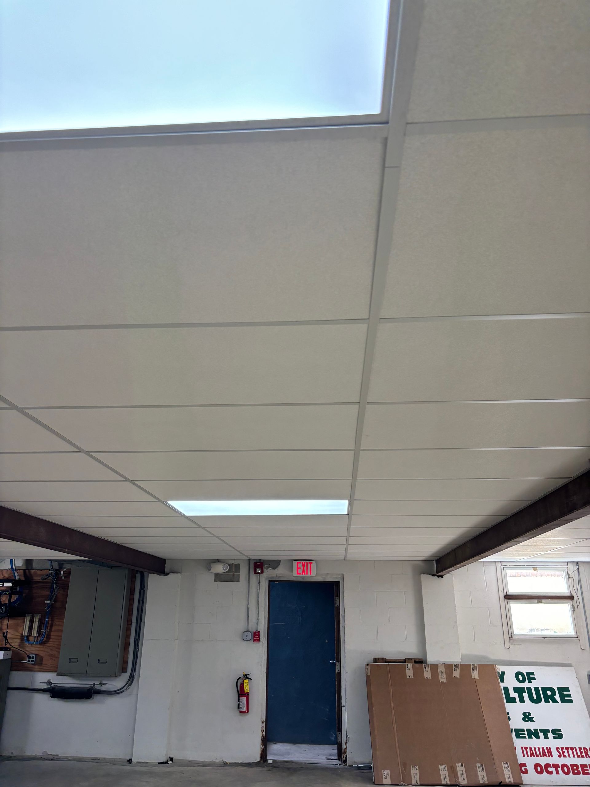 Low-angle view of a room with a drop ceiling, exit sign, and cardboard boxes. Light coming from skylights.