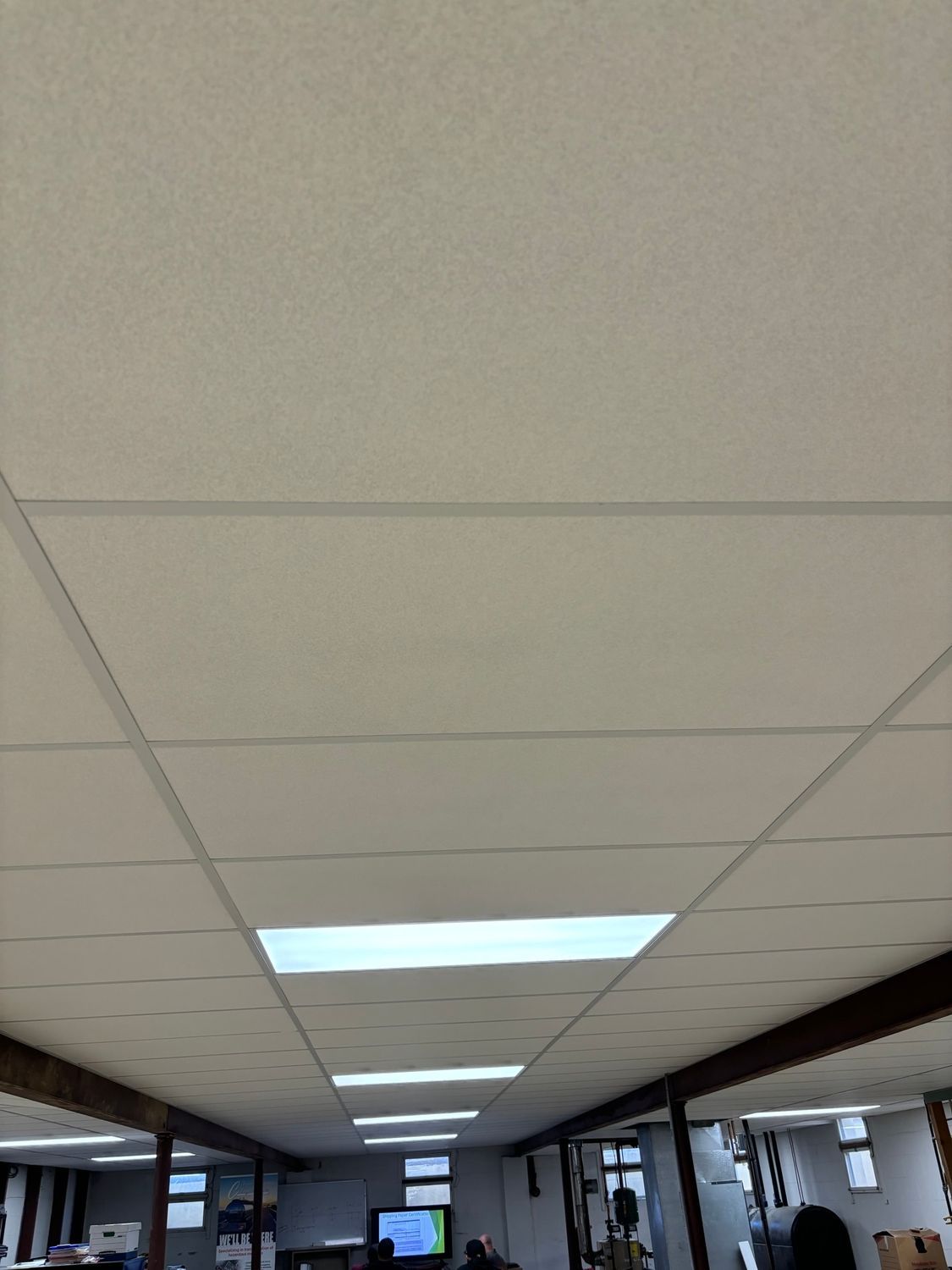 Suspended ceiling with rectangular light fixtures and dark support beams, view from below.